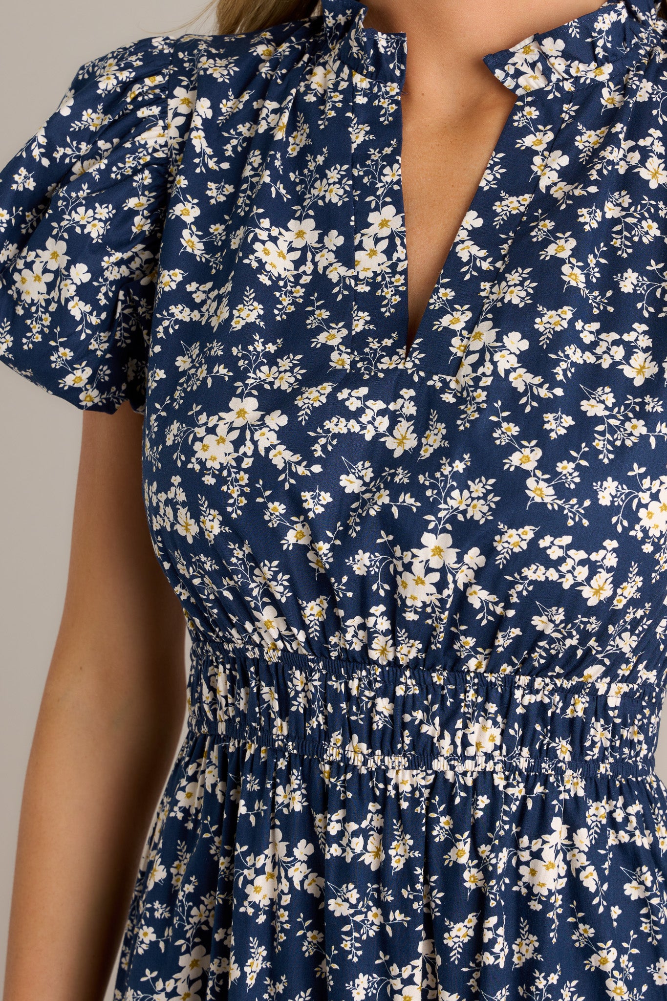 Close-up of the navy floral dress showing the v-neckline, ruffle collar, and floral pattern.