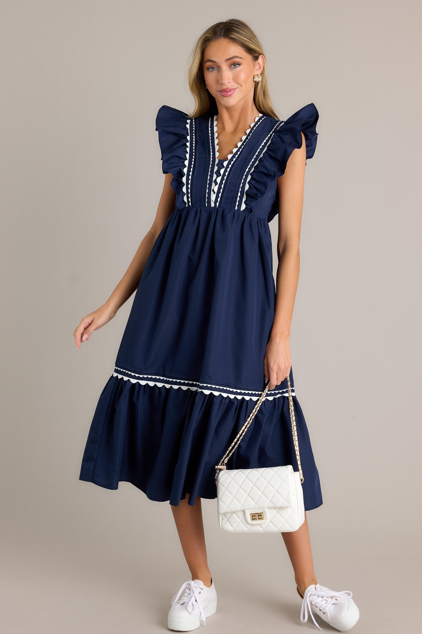 This navy midi dress features a v-neckline, a discrete side zipper, scalloped &amp; ruffled bodice detailing, functional hip pockets, and short flutter sleeves.