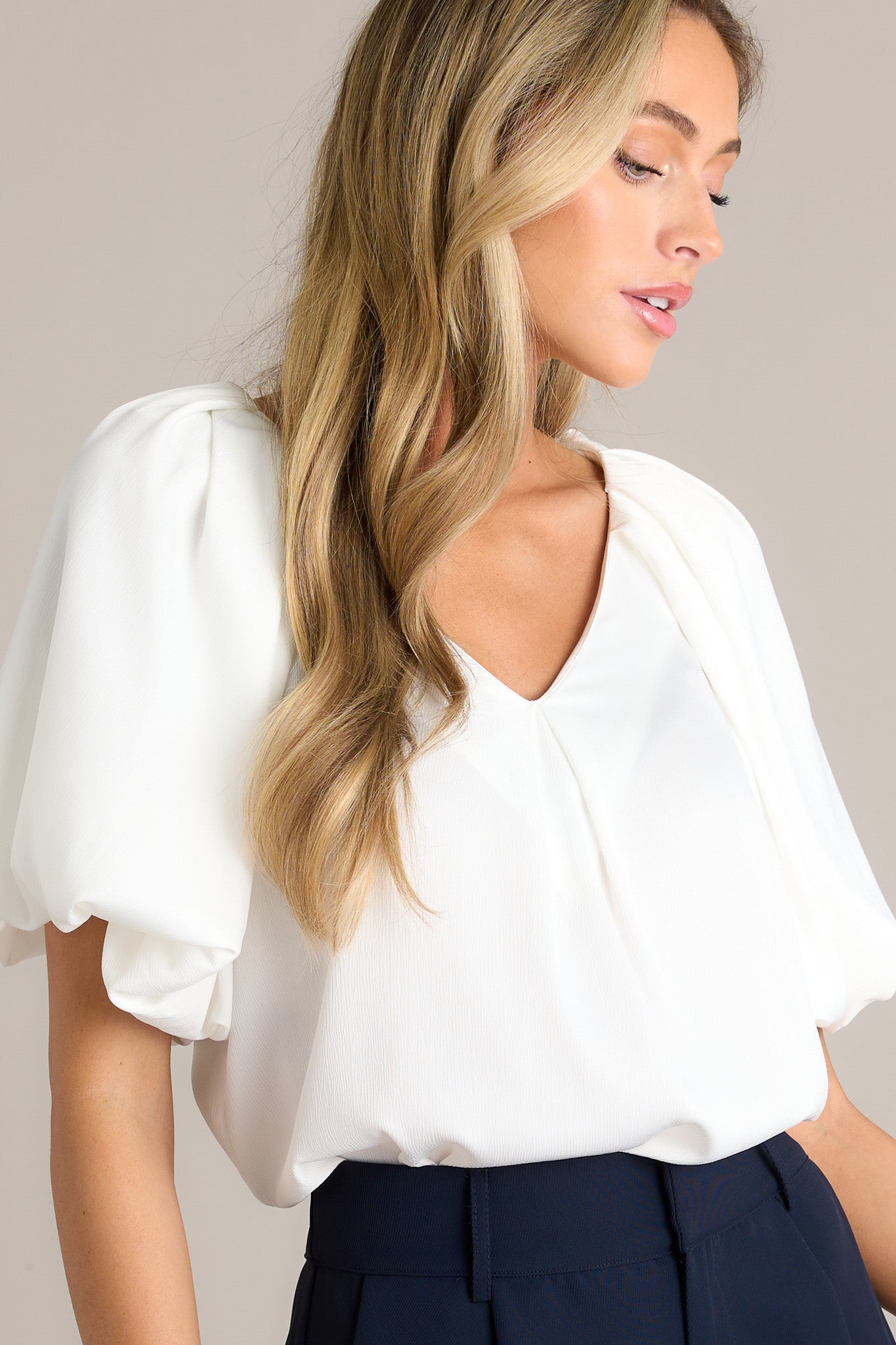 Close up view of an ivory blouse with a v neckline and puff sleeves.