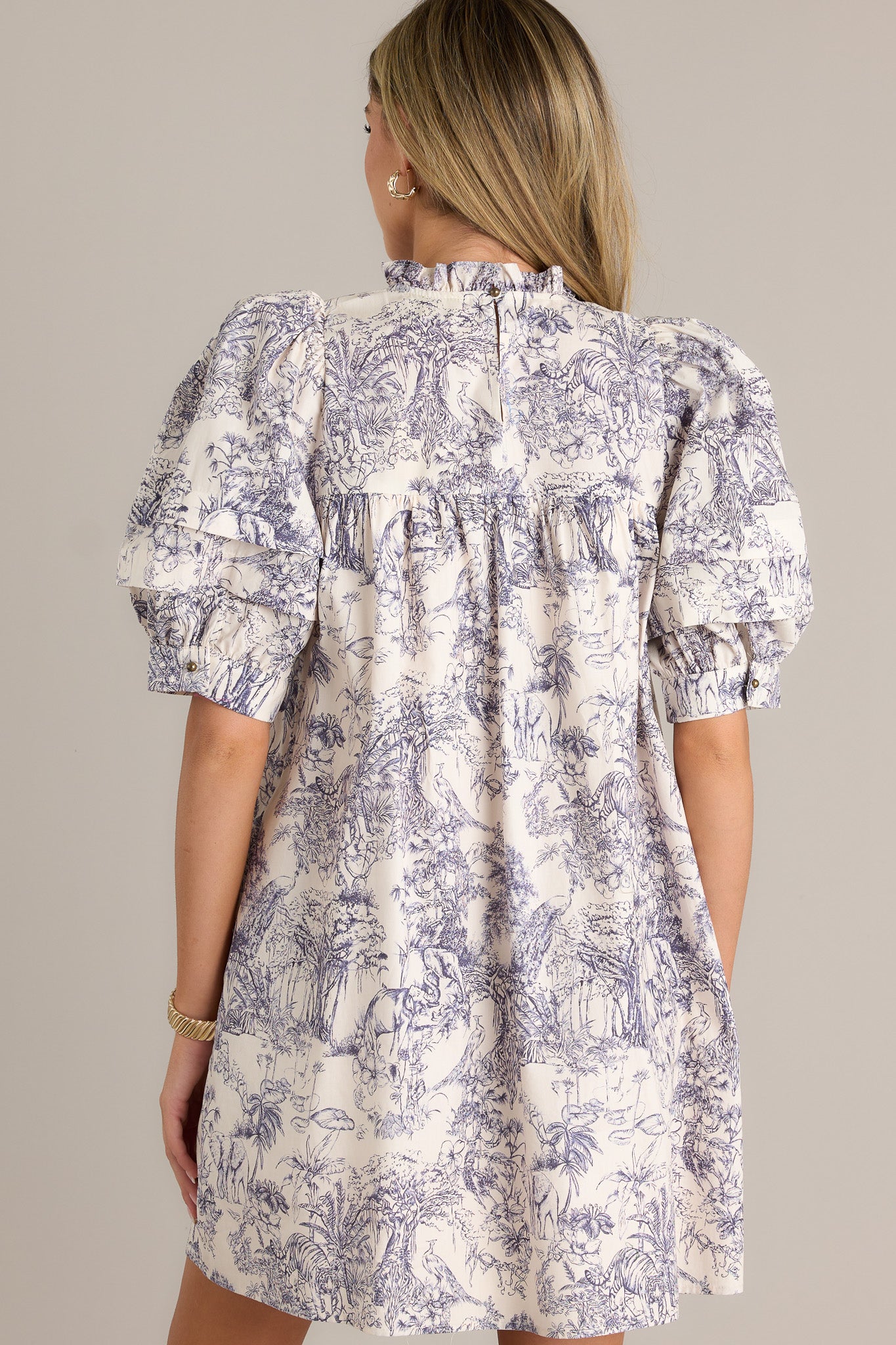 Back view of a navy toile mini dress highlighting the overall fit, unique toile pattern, and button cuffed puff sleeves.