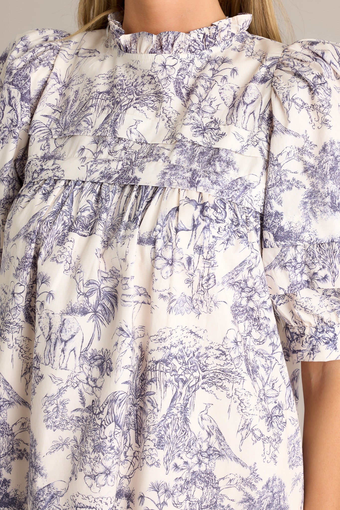 Close-up of the navy toile mini dress showing the high ruffled neckline, subtle chest pleats, and unique toile pattern.