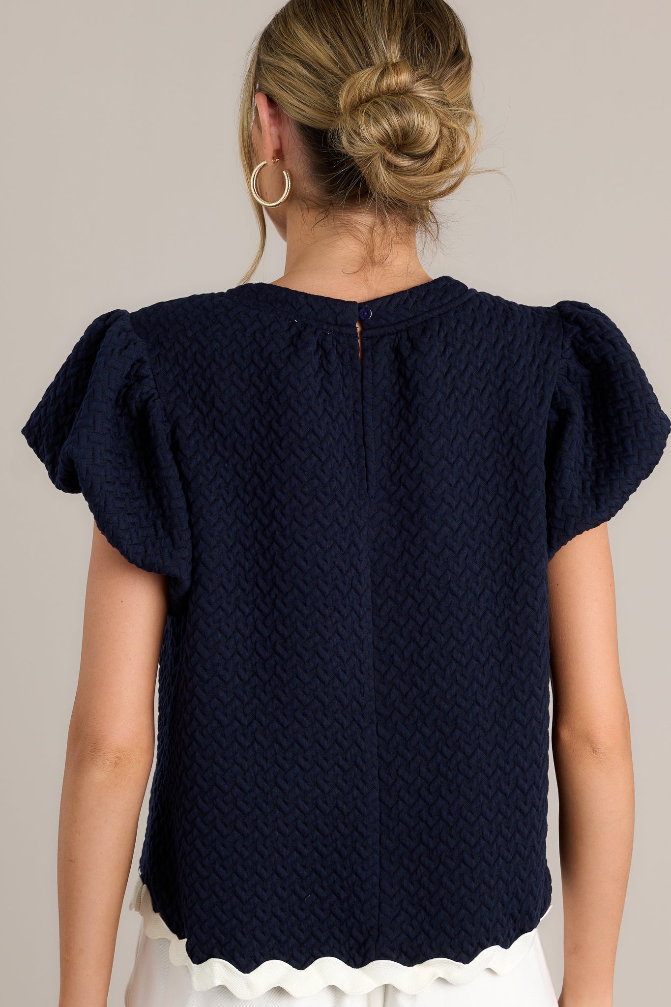 Back view of a navy top highlighting the overall fit, quilted material, and contrasting scalloped hemline.