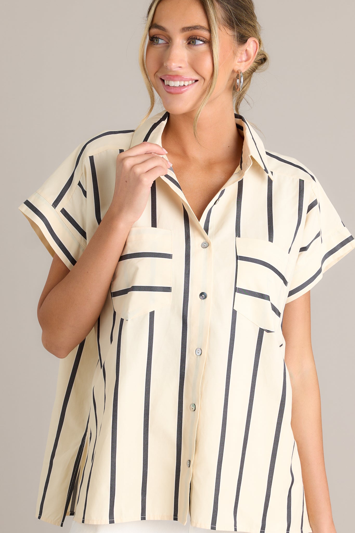 Front view of a black stripe top featuring a collared neckline, functional breast pockets, a full button front, a split hemline, and short sleeves.