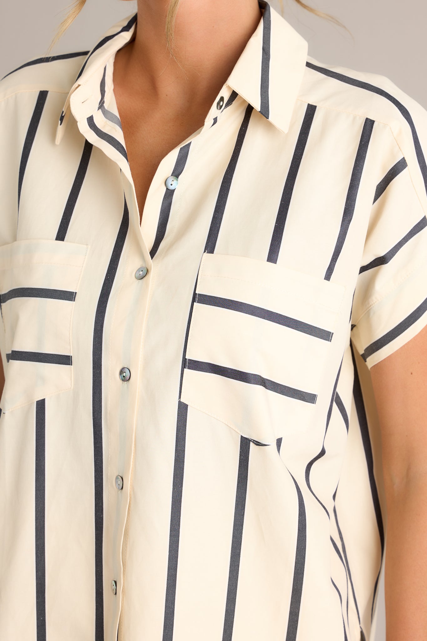 Close-up of the black stripe top showing the collared neckline, functional breast pockets, and full button front.