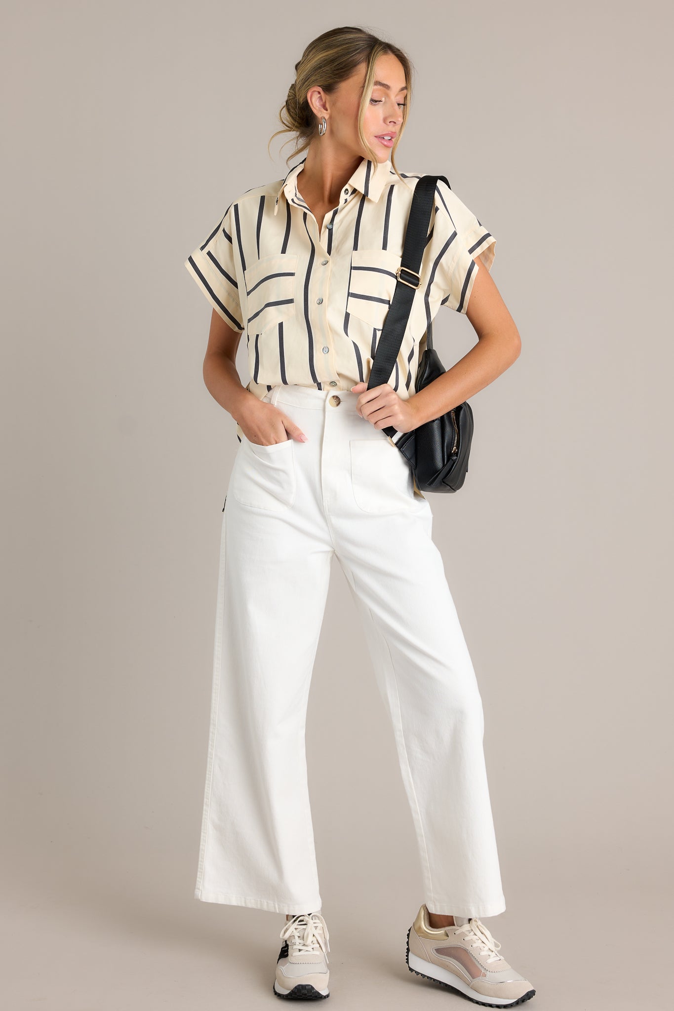 Front angled view of a black stripe top featuring a collared neckline, functional breast pockets, a full button front, a split hemline, and short sleeves