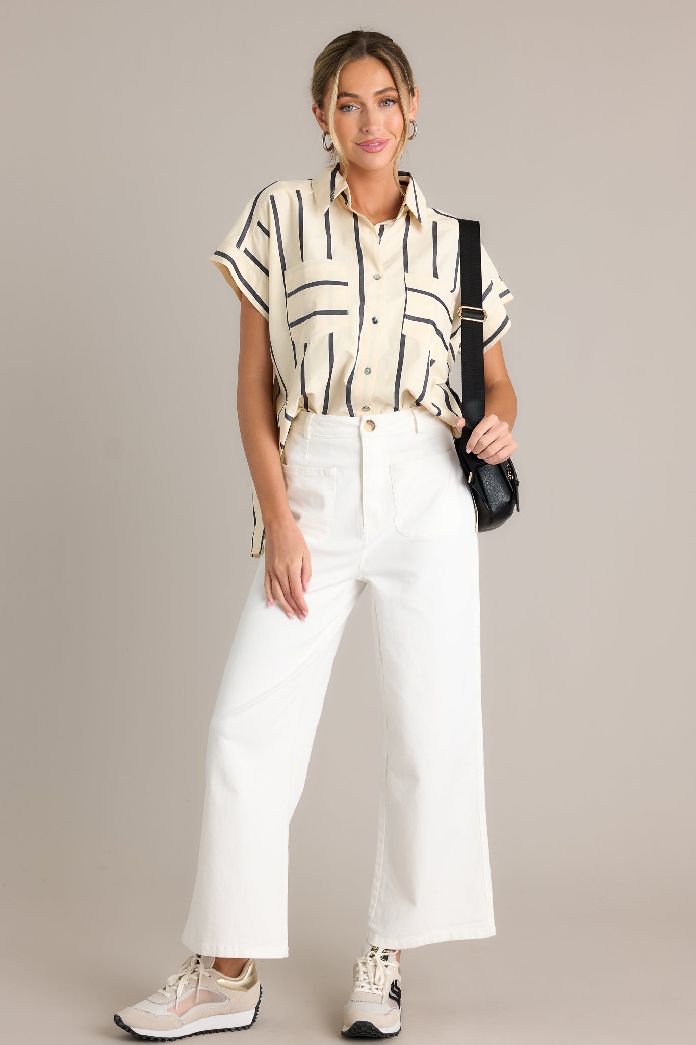 Full length view of a black stripe top with a collared neckline, functional breast pockets, a full button front, a split hemline, and short sleeves