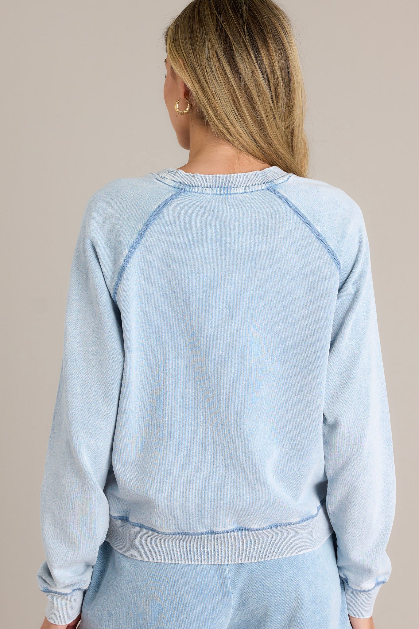 Back view of this denim top that features a crew neckline, dropped shoulders, exposed seams, and a split ribbed hemline