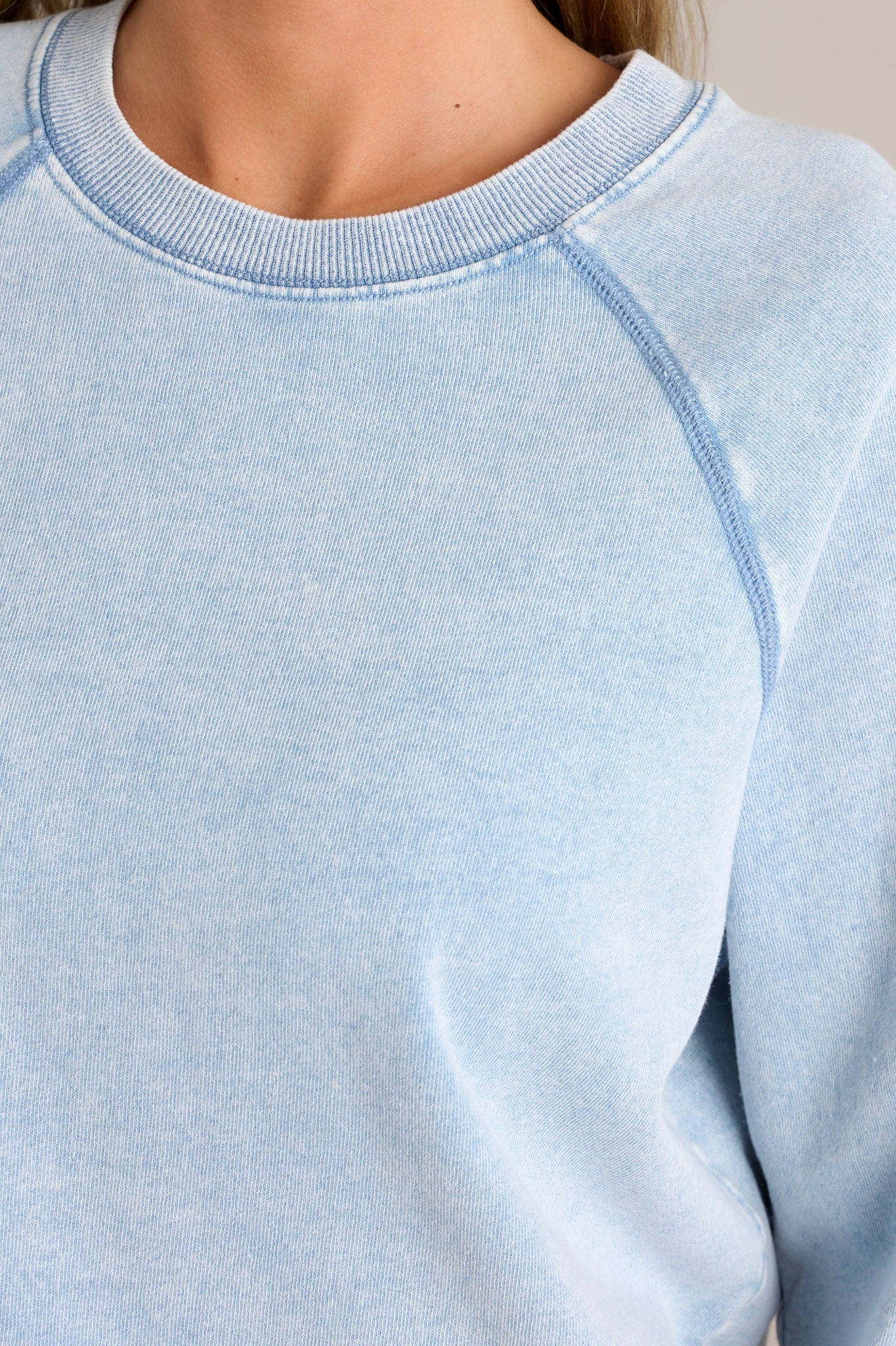 Close-up view of this denim top that features a crew neckline, dropped shoulders, exposed seams, and a split ribbed hemline