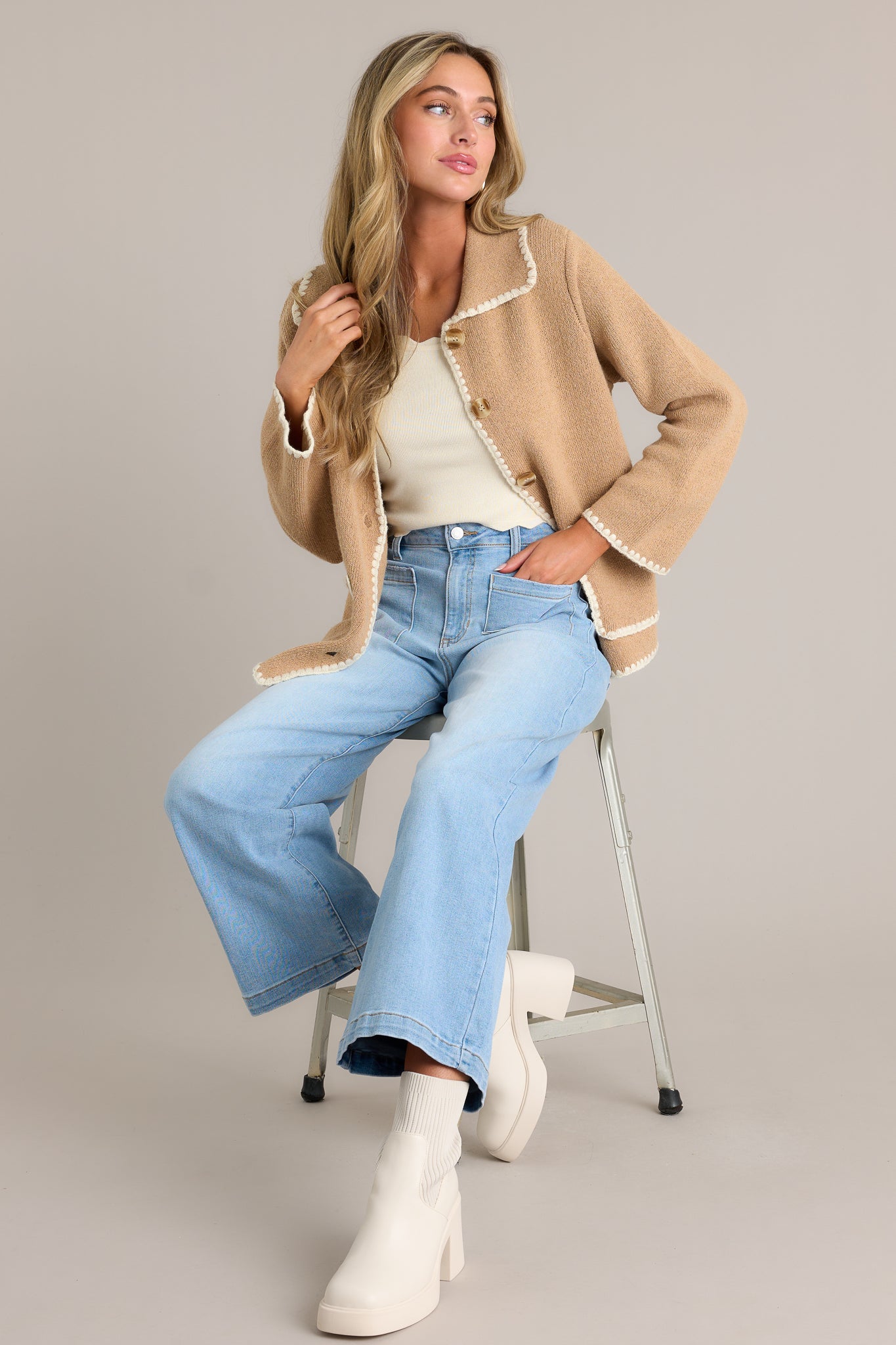 Side view of a tan jacket showcasing the collared neckline, full button front, functional pockets, and ivory knitted trim.