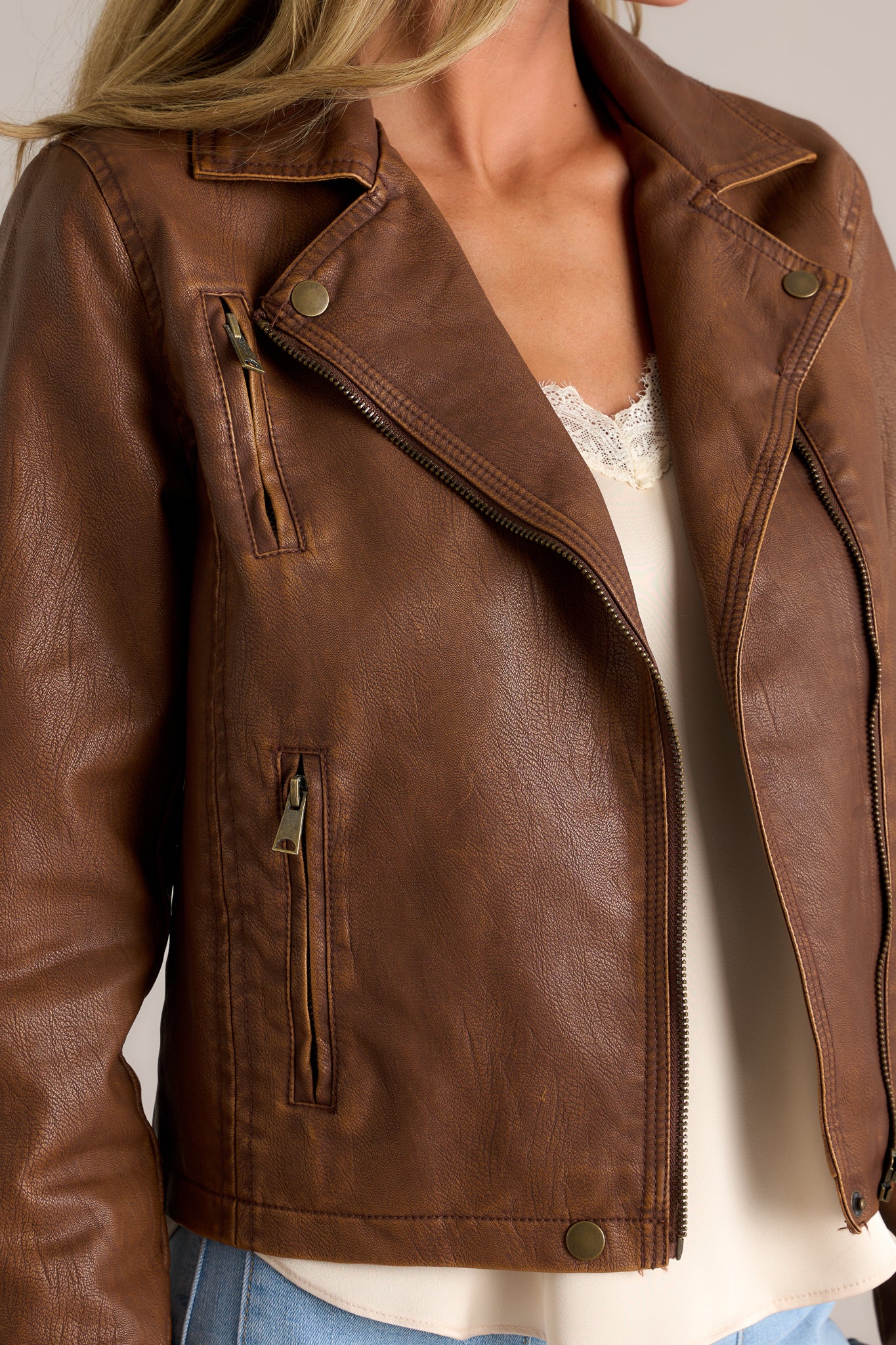 Close-up of the jacket showing the washed gold hardware, collar neckline with snap buttons, front functional zipper, and one of the three functional zipper pockets.