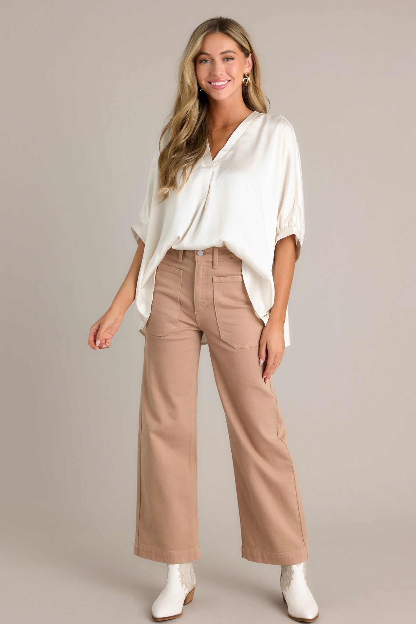 Front view of a white top featuring a v-neckline, short dolman sleeves with pleated detailing, a wide, flowy fit, and a satin-like material throughout.