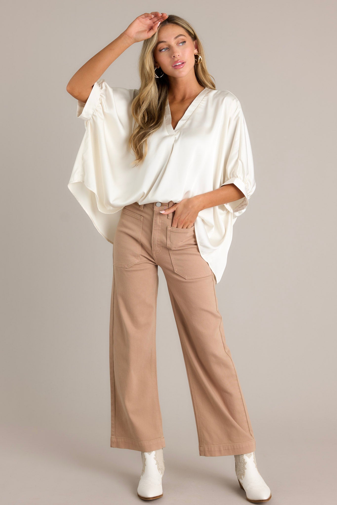 Full length view of a white top with a v-neckline, short dolman sleeves with pleated detailing, a wide, flowy fit, and a satin-like material