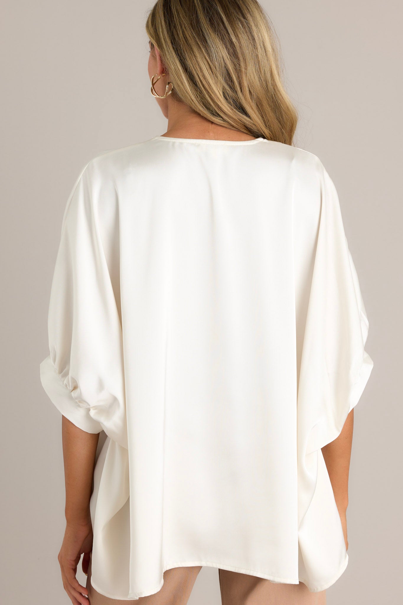 Back view of a white top highlighting the overall fit, wide, flowy design, and satin-like material.