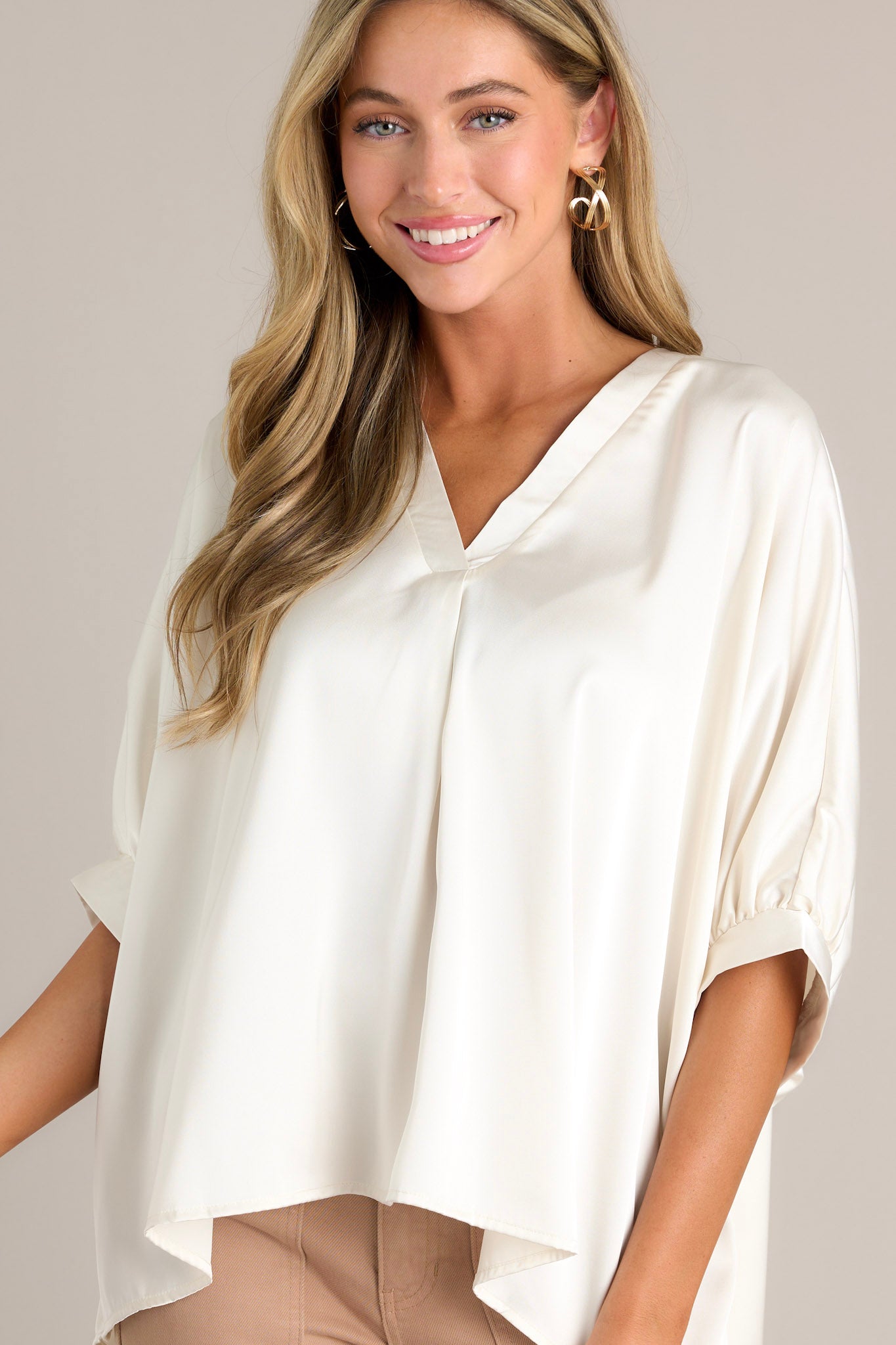 This white top features a v-neckline, short dolman sleeves with pleated detailing, a wide, flowy fit, and a satin-like material throughout.