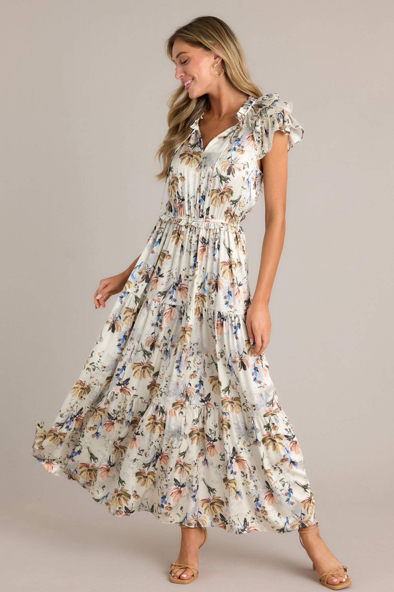 Action shot of an ivory floral dress displaying the fit and movement, highlighting the v-neckline, self-tie drawstring, floral pattern, tiered design, tiered sleeves, and flowing silhouette.