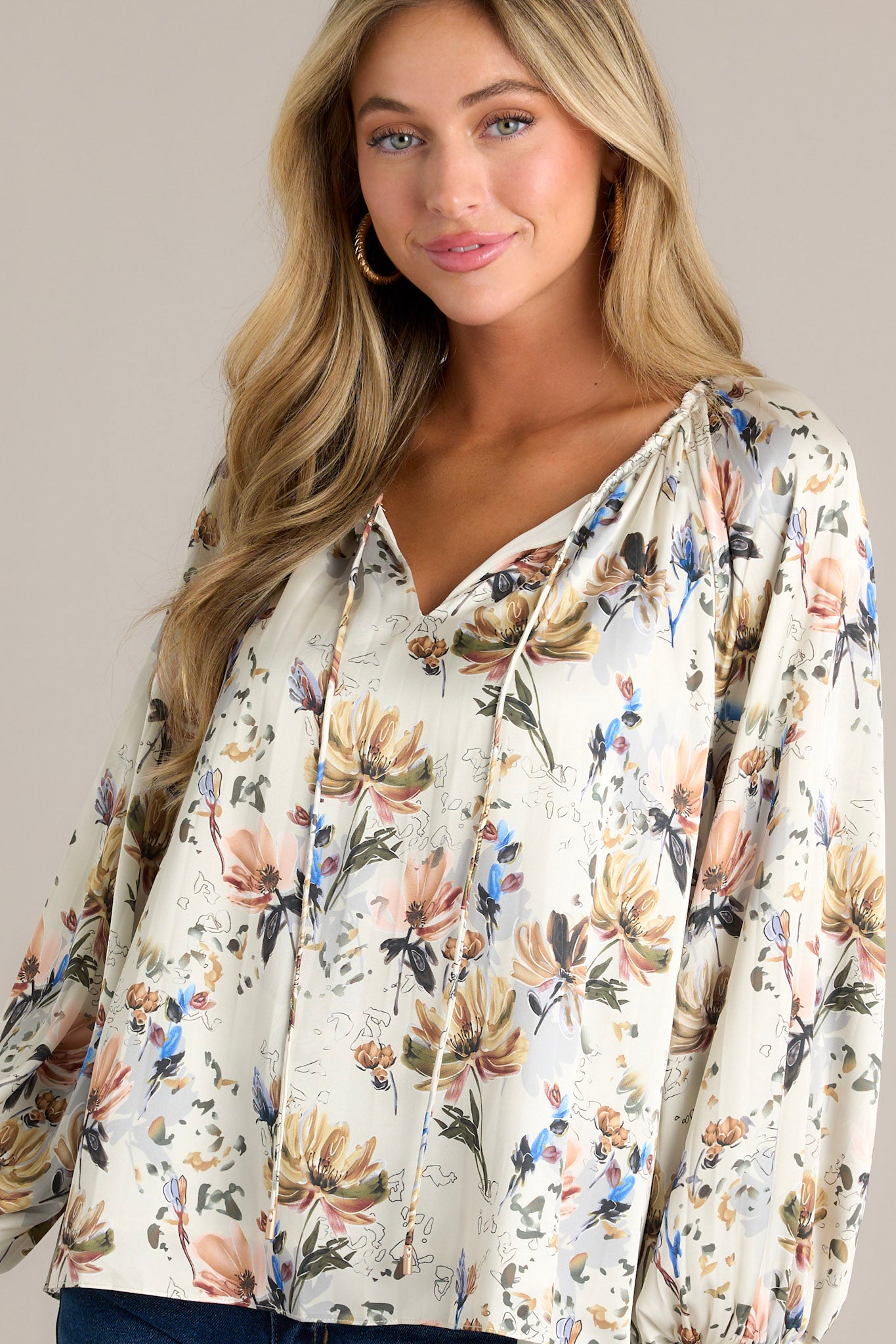 This ivory floral blouse features a v-neckline with a self-tie drawstring, a lined bodice, balloon sleeves with smocked cuffs and a pleated design.