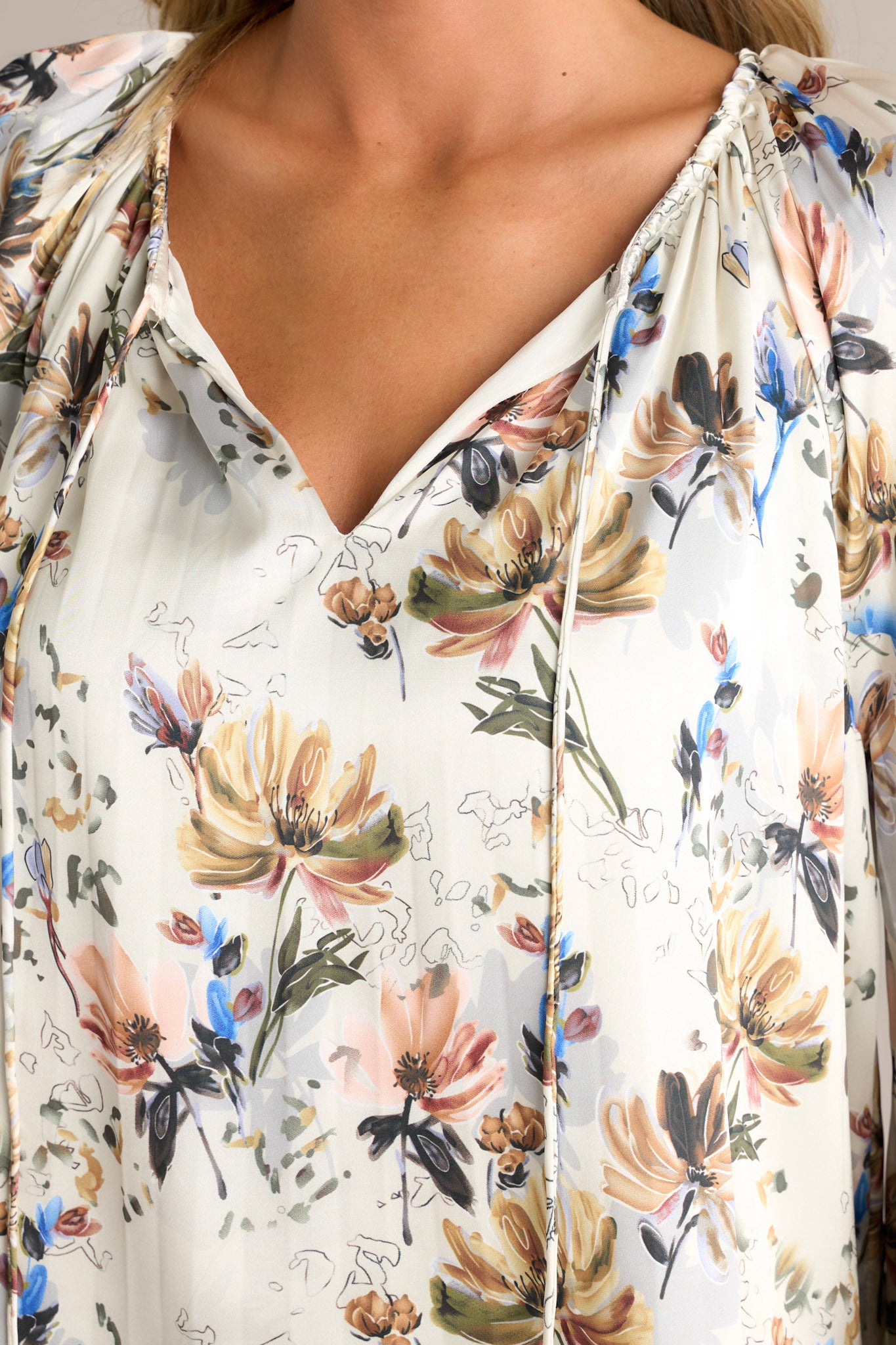 Close-up of the ivory floral blouse showing the v-neckline with self-tie drawstring, lined bodice, and pleated design.