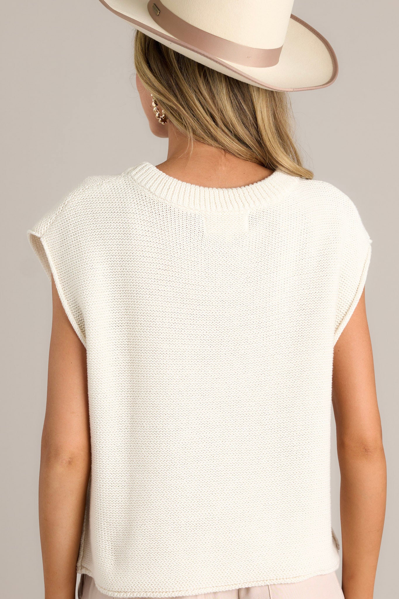 Back view of an ivory sweater top featuring a ribbed crew neckline, wide sleeves, knitted material, and a folded hemline.