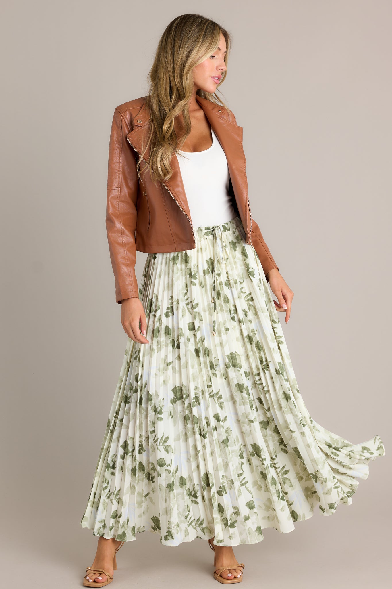 Action shot of a green skirt with a high waisted design, an elastic waistband, a self-tie drawstring with bead detailing, pleats throughout, and a flowing silhouette, highlighting the flow and movement of the skirt.