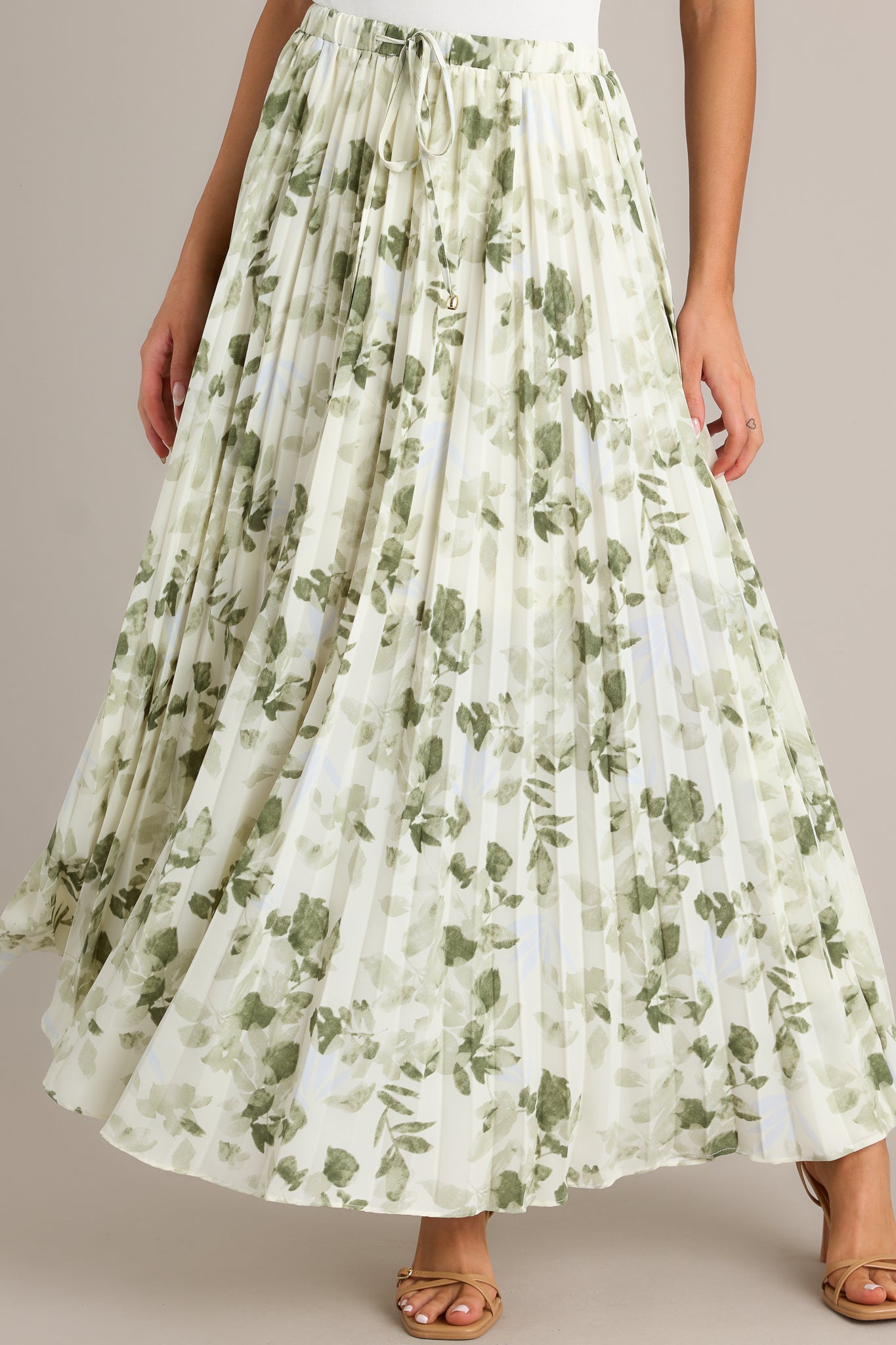 Angled front view of a green skirt featuring a high waisted design, an elastic waistband, a self-tie drawstring with bead detailing, pleats throughout, and a flowing silhouette.