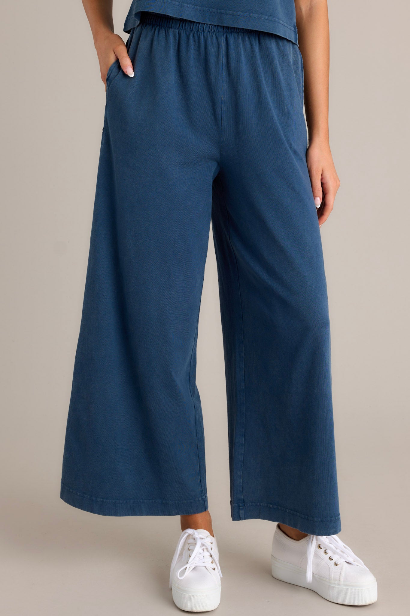 Front angled view of blue flare pants featuring an elastic waistband, functional pockets, a wide leg design, and a soft jersey material