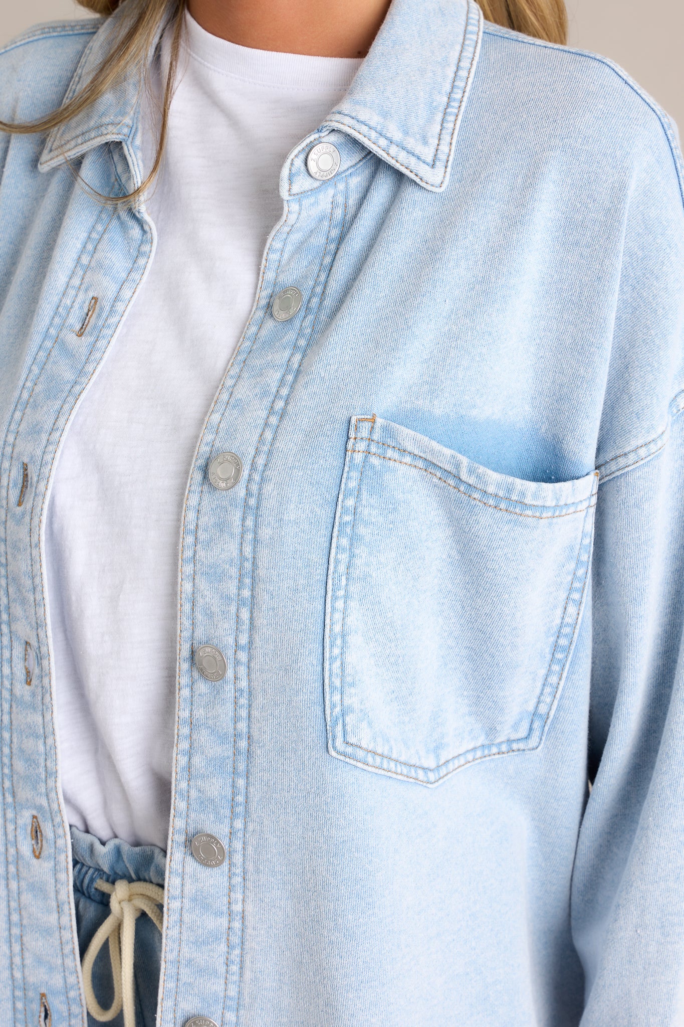 Close-up of the denim jacket showing the functional button front, curved hemline, and one of the functional breast pockets.