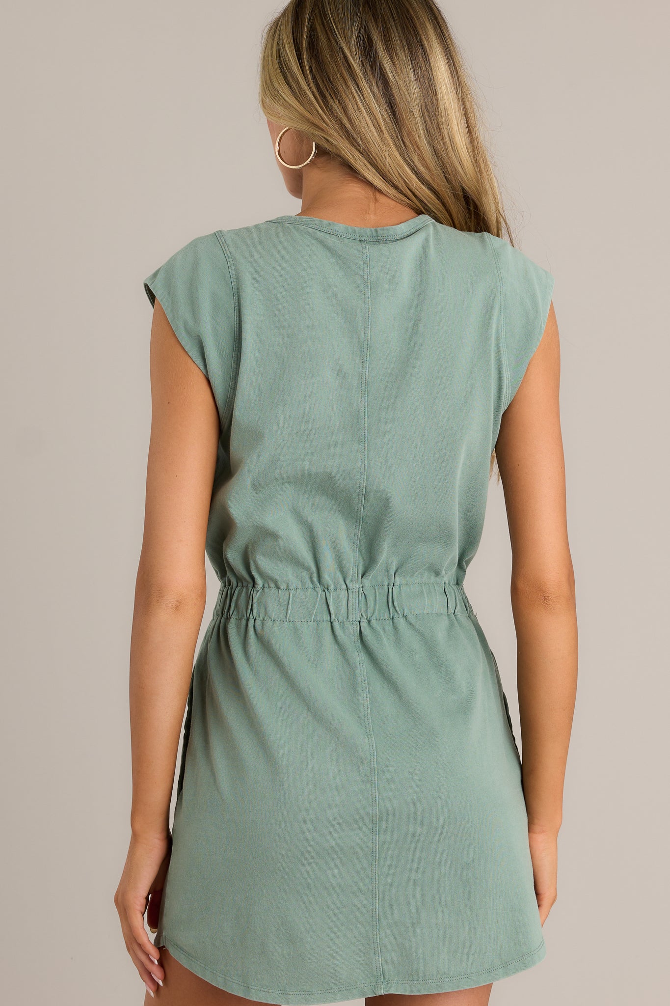 Back view of a green mini dress highlighting the overall fit, elastic waistband, and short cap sleeves.