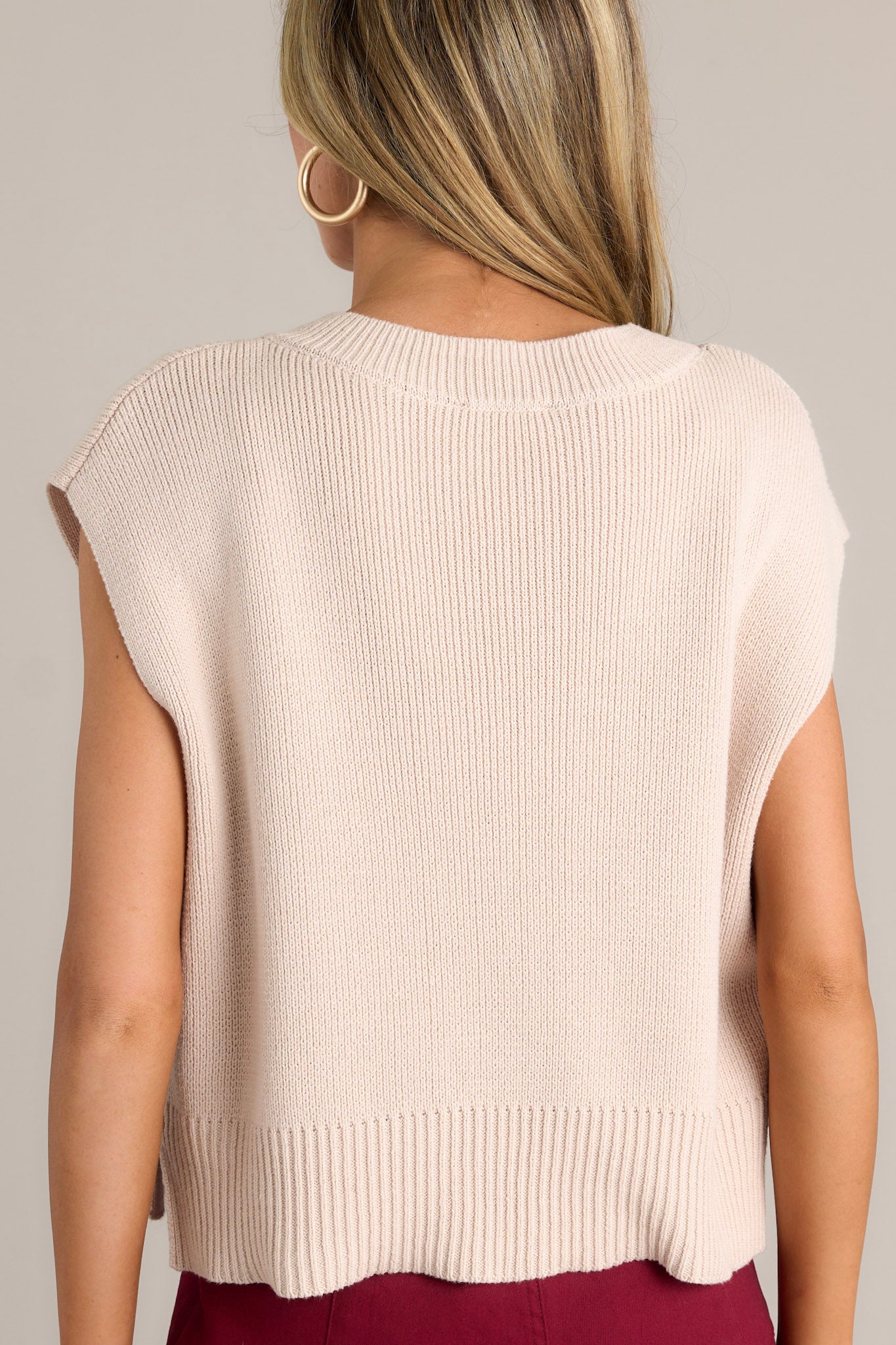 The back of the beige sweater top displaying the knit material, thick hemline, and side slits in the hem.