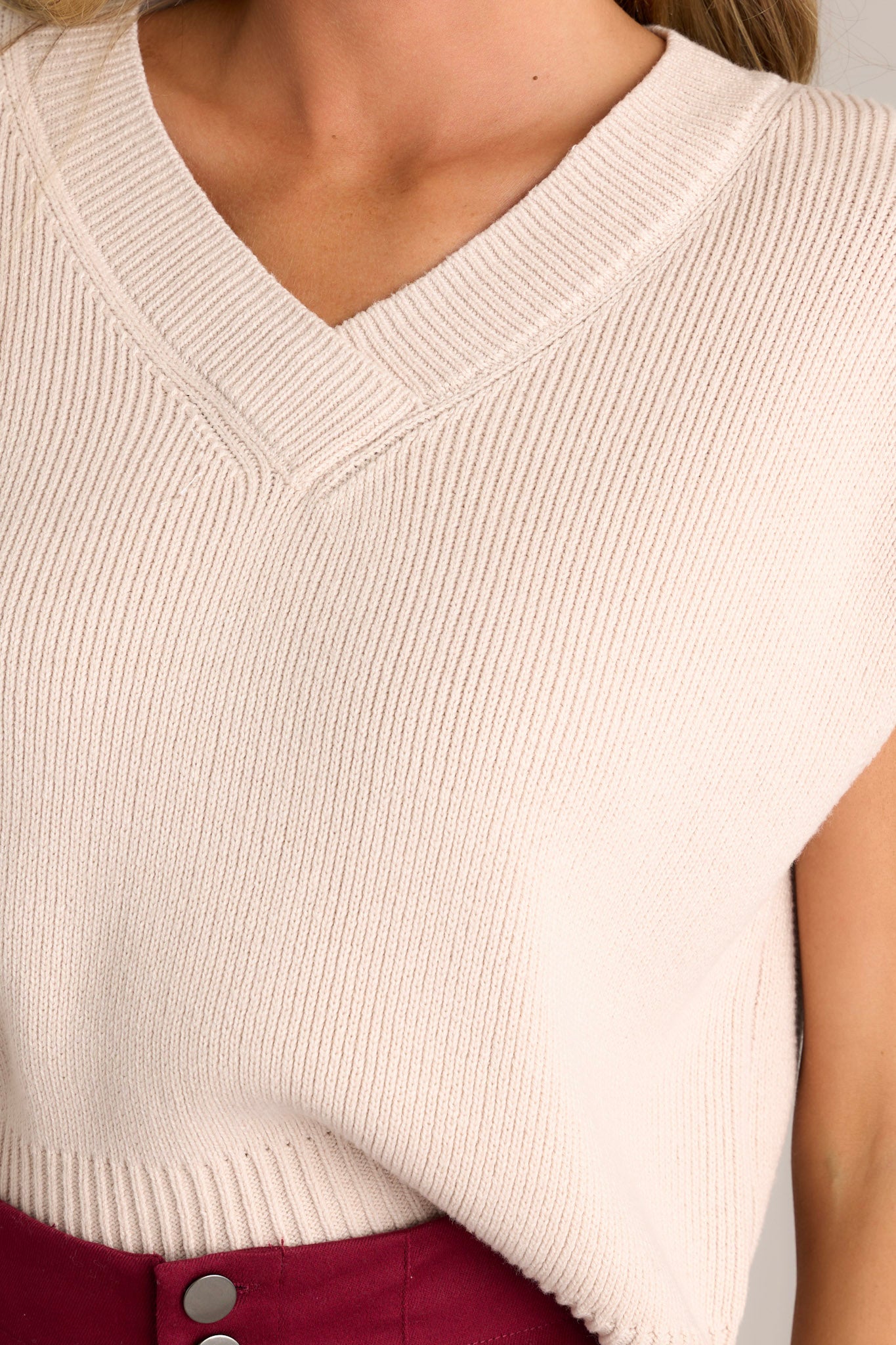 Close-up of the beige sweater top's knit material, showcasing the thick hemline and side slits in the hem.