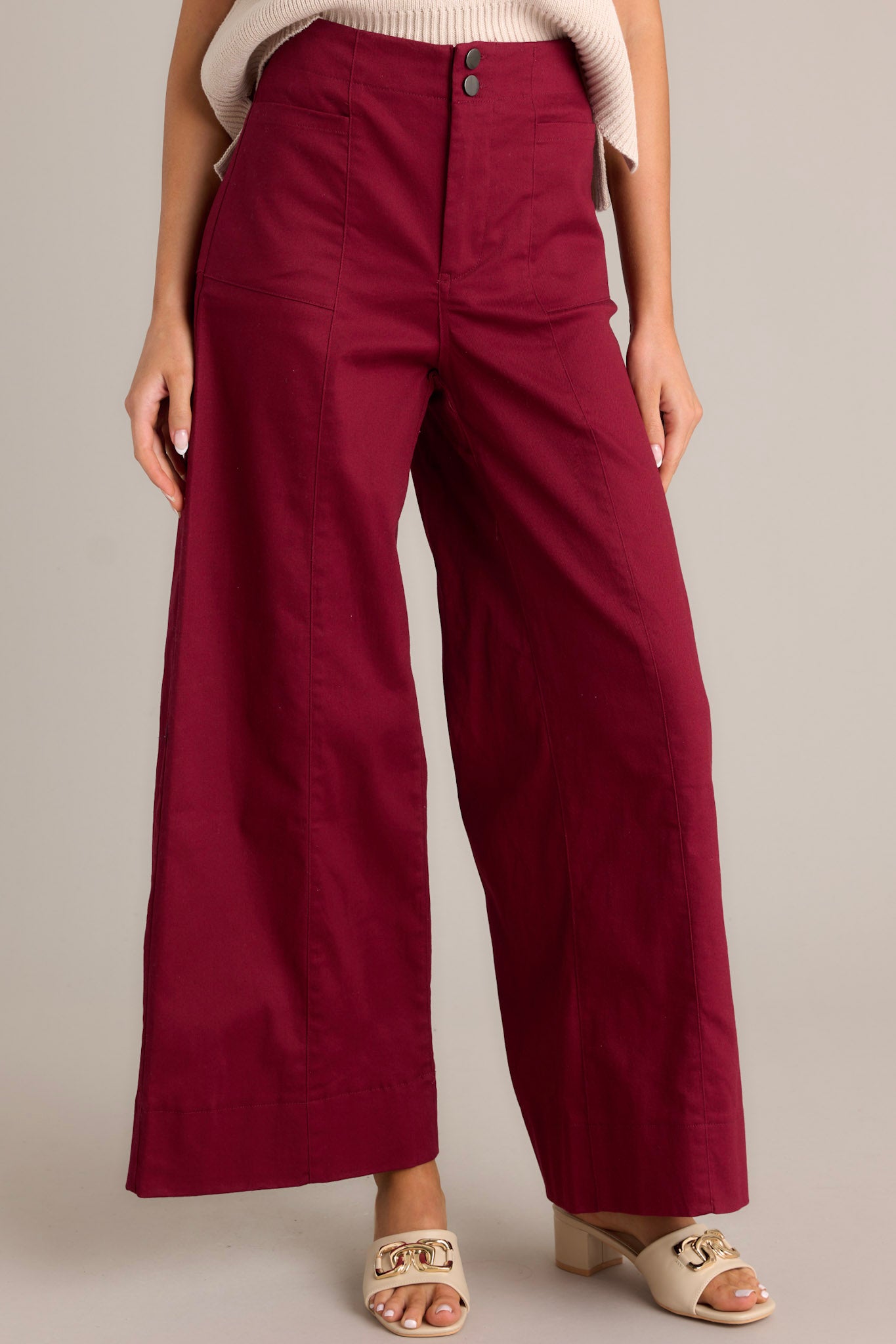 Front view of burgundy pants featuring a high waisted design, a button zipper closure, functional rectangular hip pockets, and a wide leg.