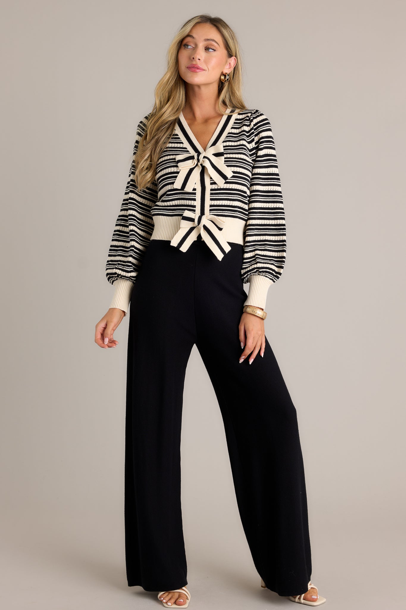 Full length view of a stripe sweater top with a v-neckline, functional snap closures, adjustable bow tie details, a classic horizontal stripe design, a thick hem, and cuffed long sleeves