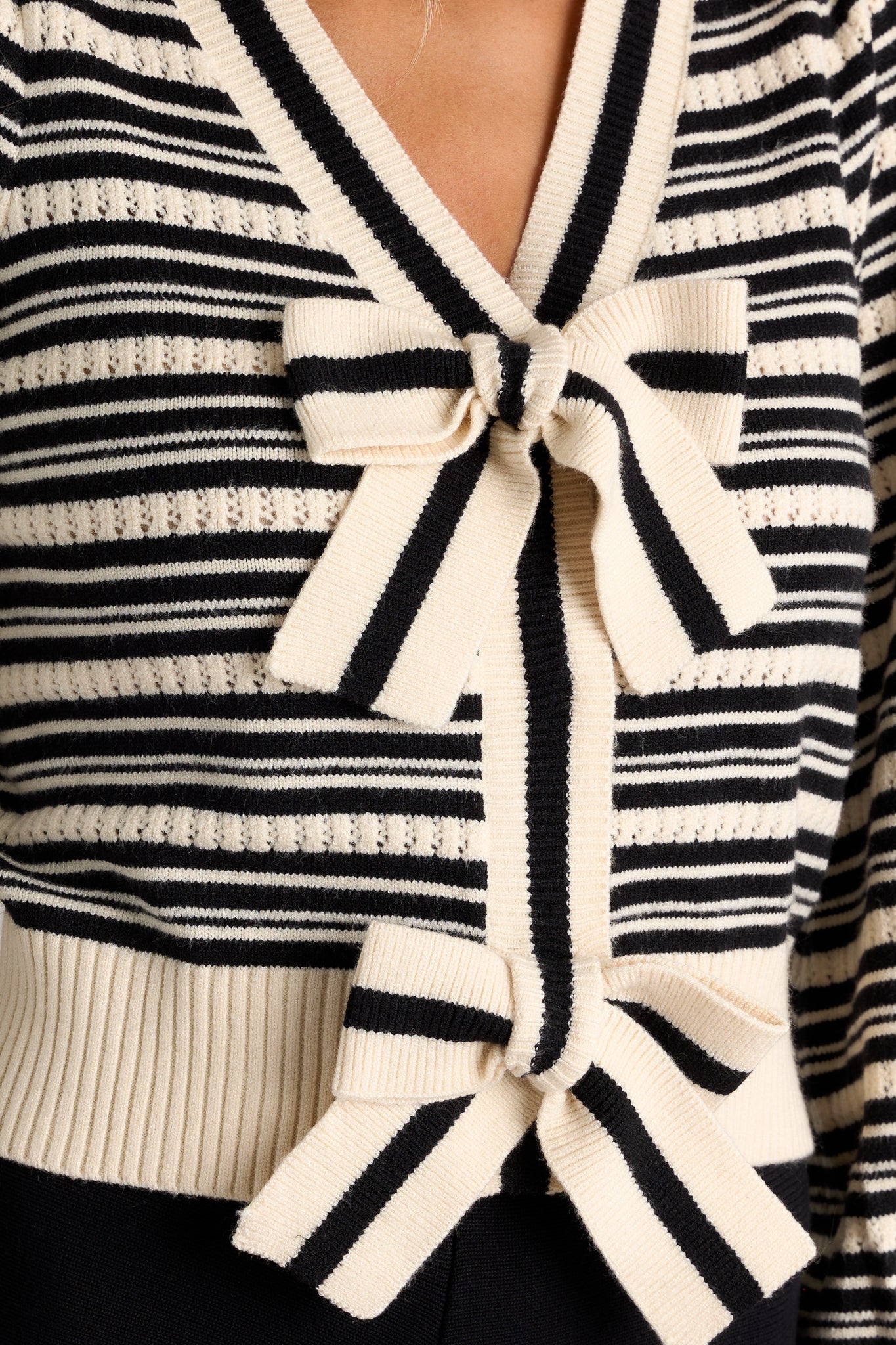 Close-up of the stripe sweater top showing the v-neckline, functional snap closures, adjustable bow tie details, and classic horizontal stripe design.