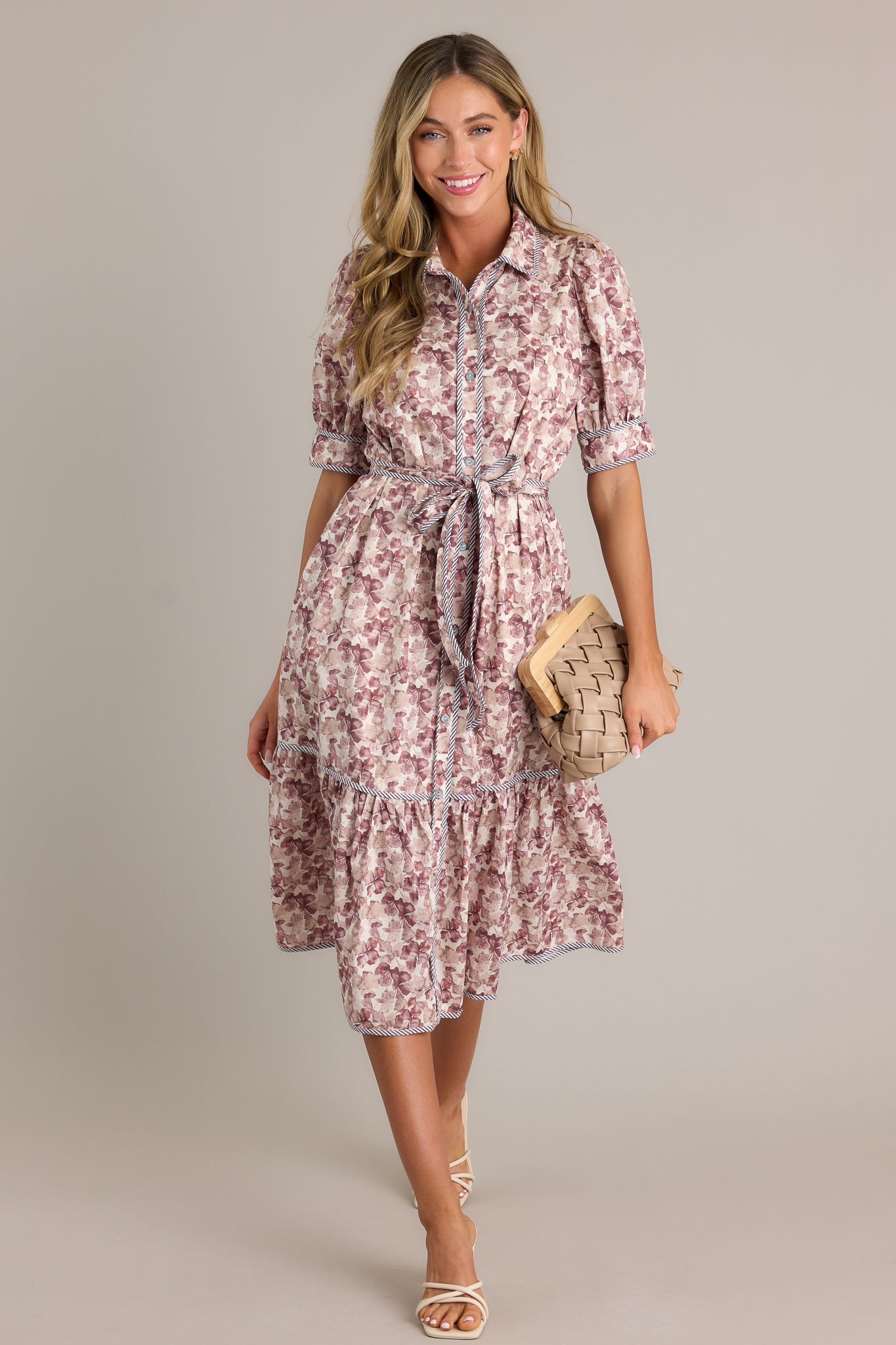 Full length view of a floral midi dress with a collared neckline, a functional button front, functional hip pockets, a self-tie belt on the waist, a tiered design, and puff sleeves