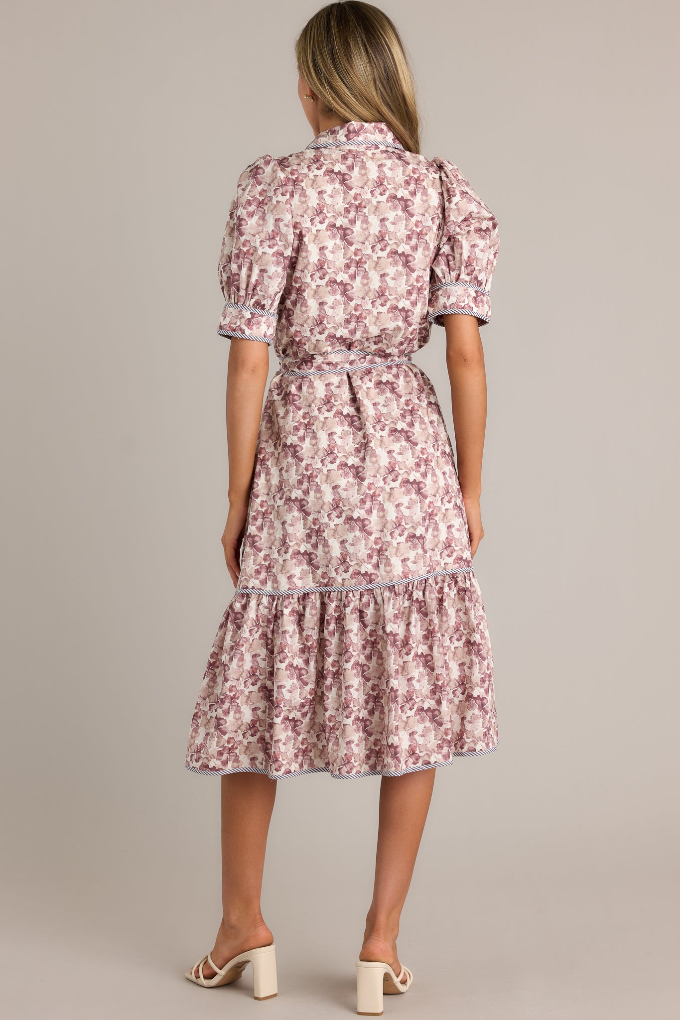 Back view of a floral midi dress highlighting the overall fit, self-tie belt on the waist, tiered design, and puff sleeves.