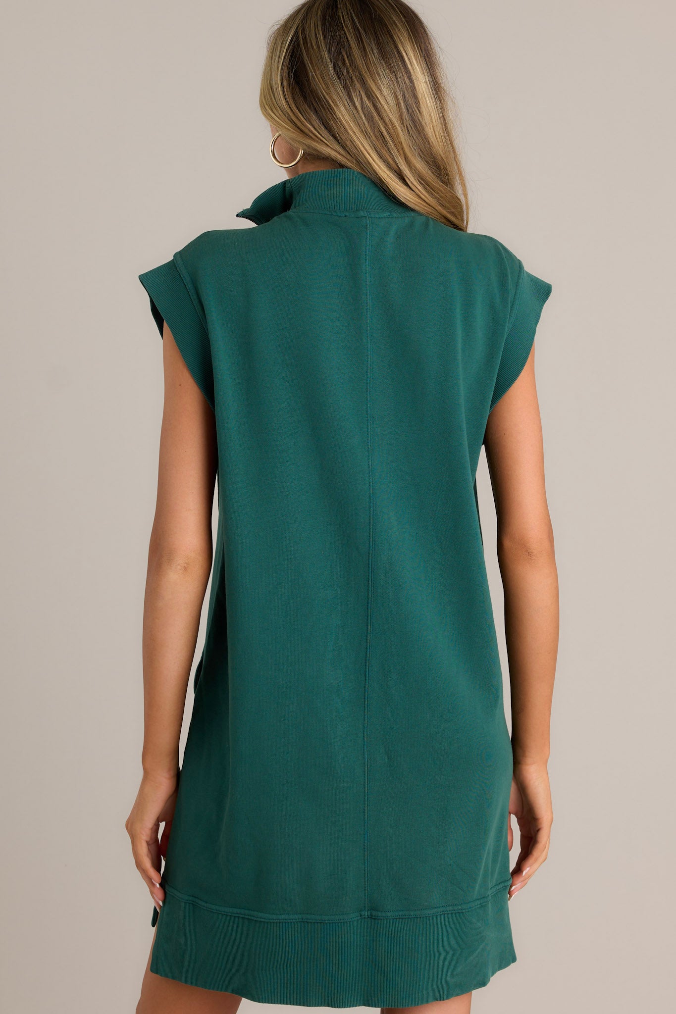 Back view of a hunter green mini dress highlighting the overall fit, ribbed detailing, split hemline, and wide ribbed sleeves.