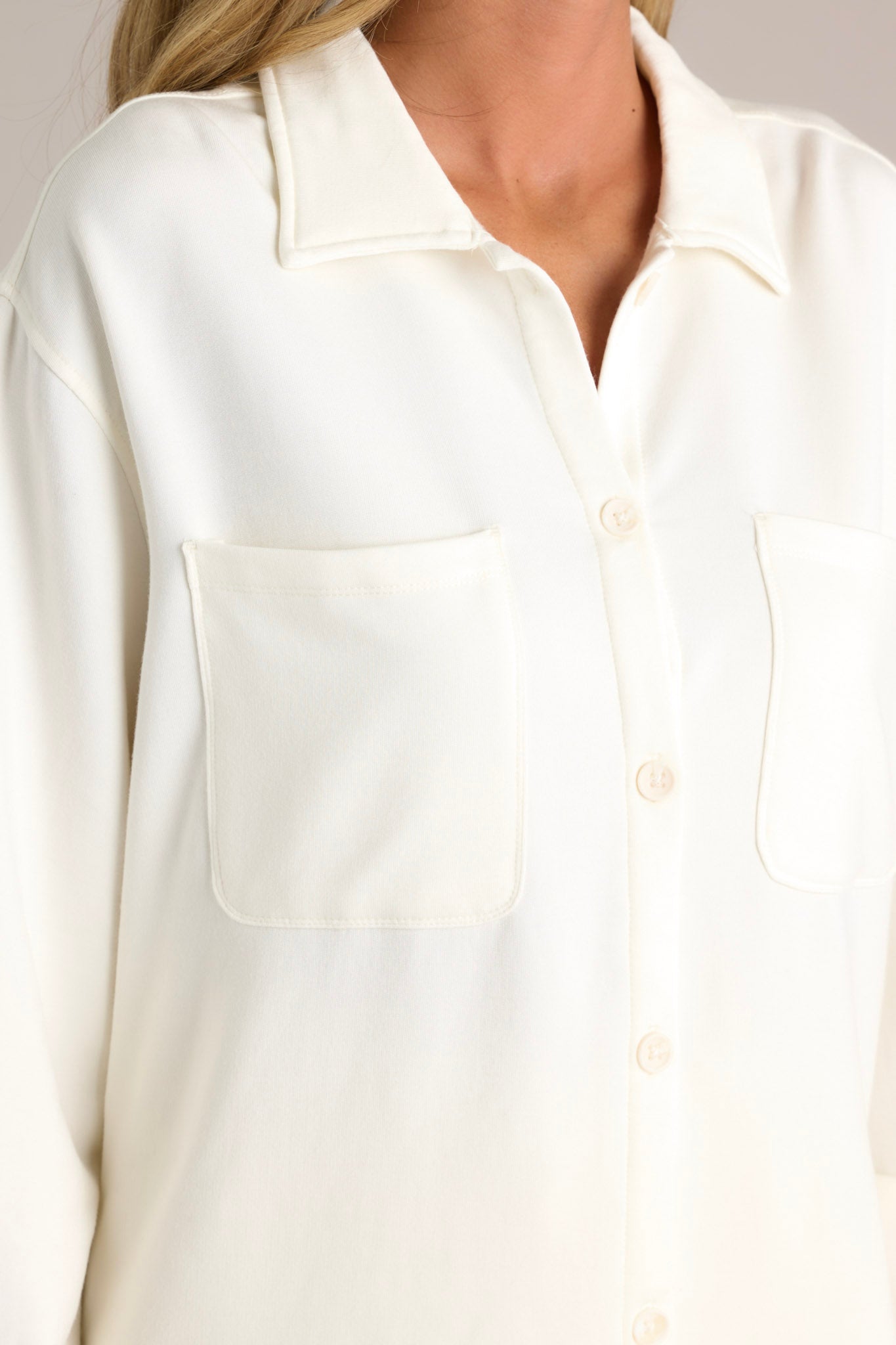 Close-up of the ivory button-up showing the collared neckline, full button front, functional breast pockets, and button-cuffed long sleeves.