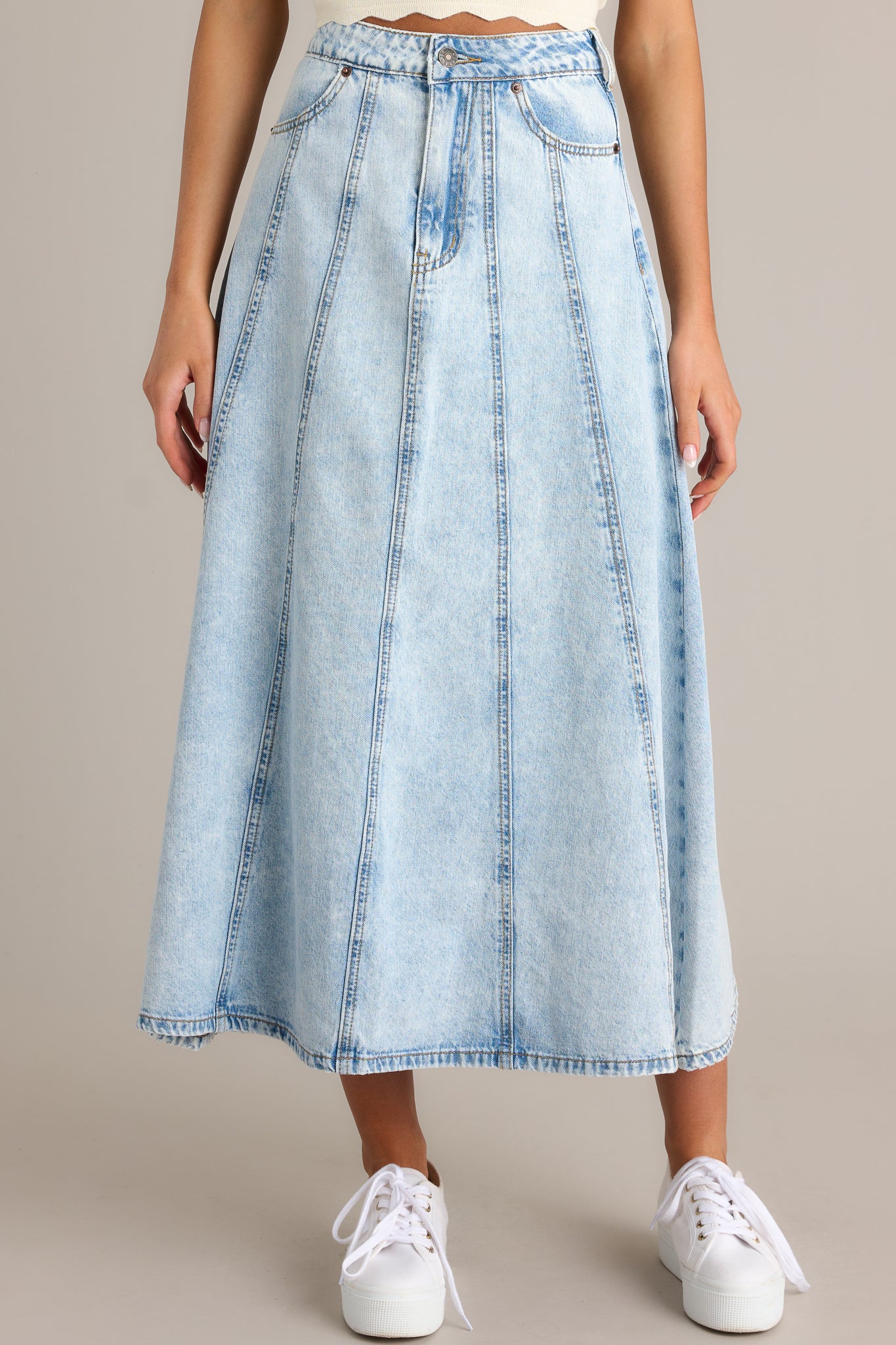 Front view of a light wash denim skirt featuring a high waisted design, functional belt loops, a button zipper closure, and functional hip and back pockets.