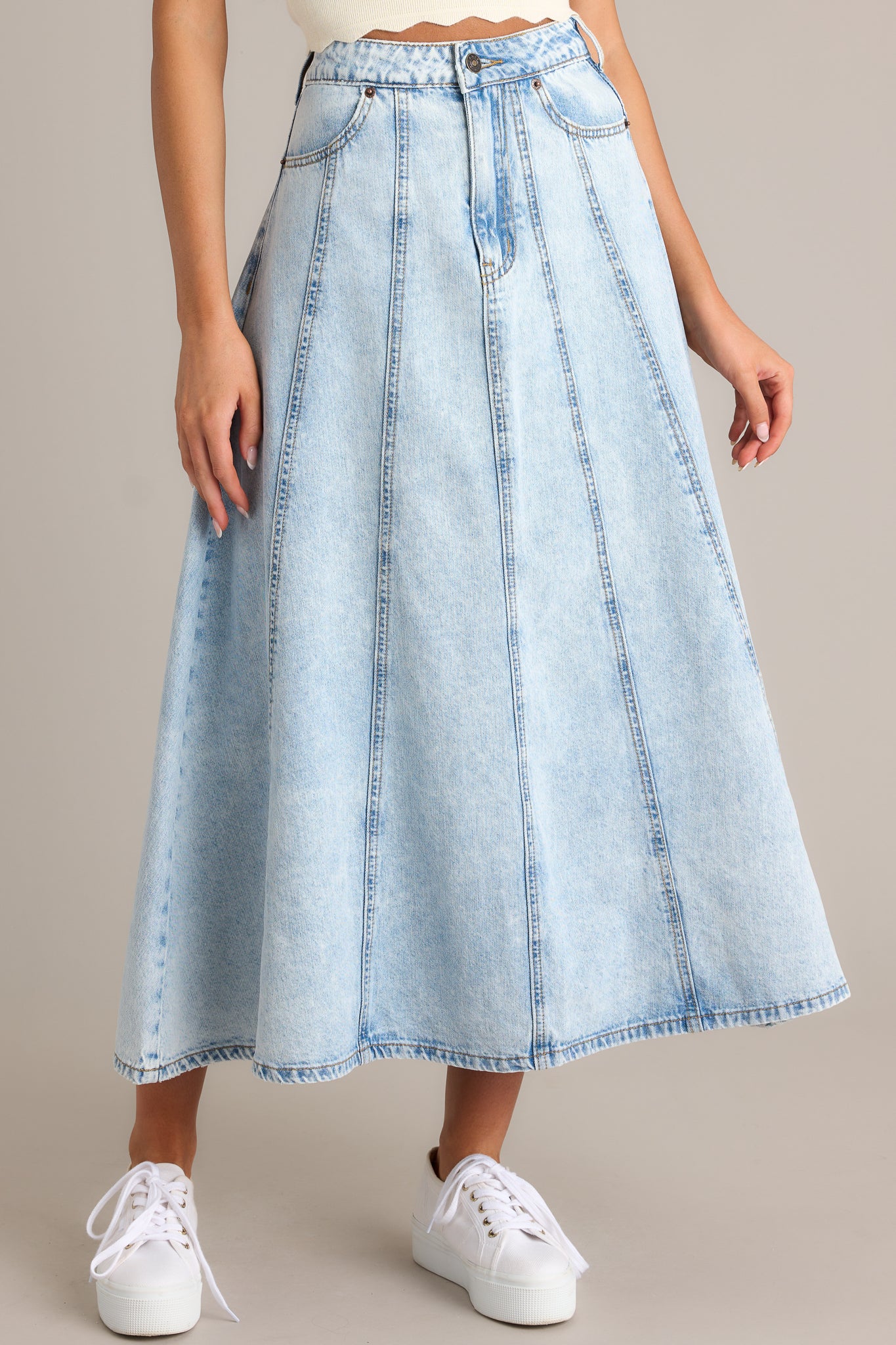 Front angled view of a light wash denim skirt featuring a high waisted design, functional belt loops, a button zipper closure, and functional hip and back pockets