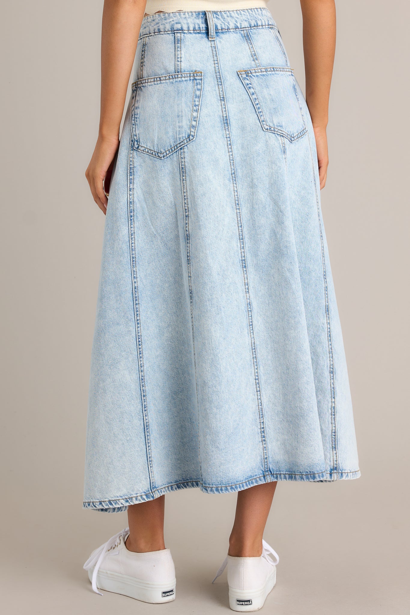 Back view of a light wash denim skirt highlighting the overall fit, functional belt loops, and back pockets.