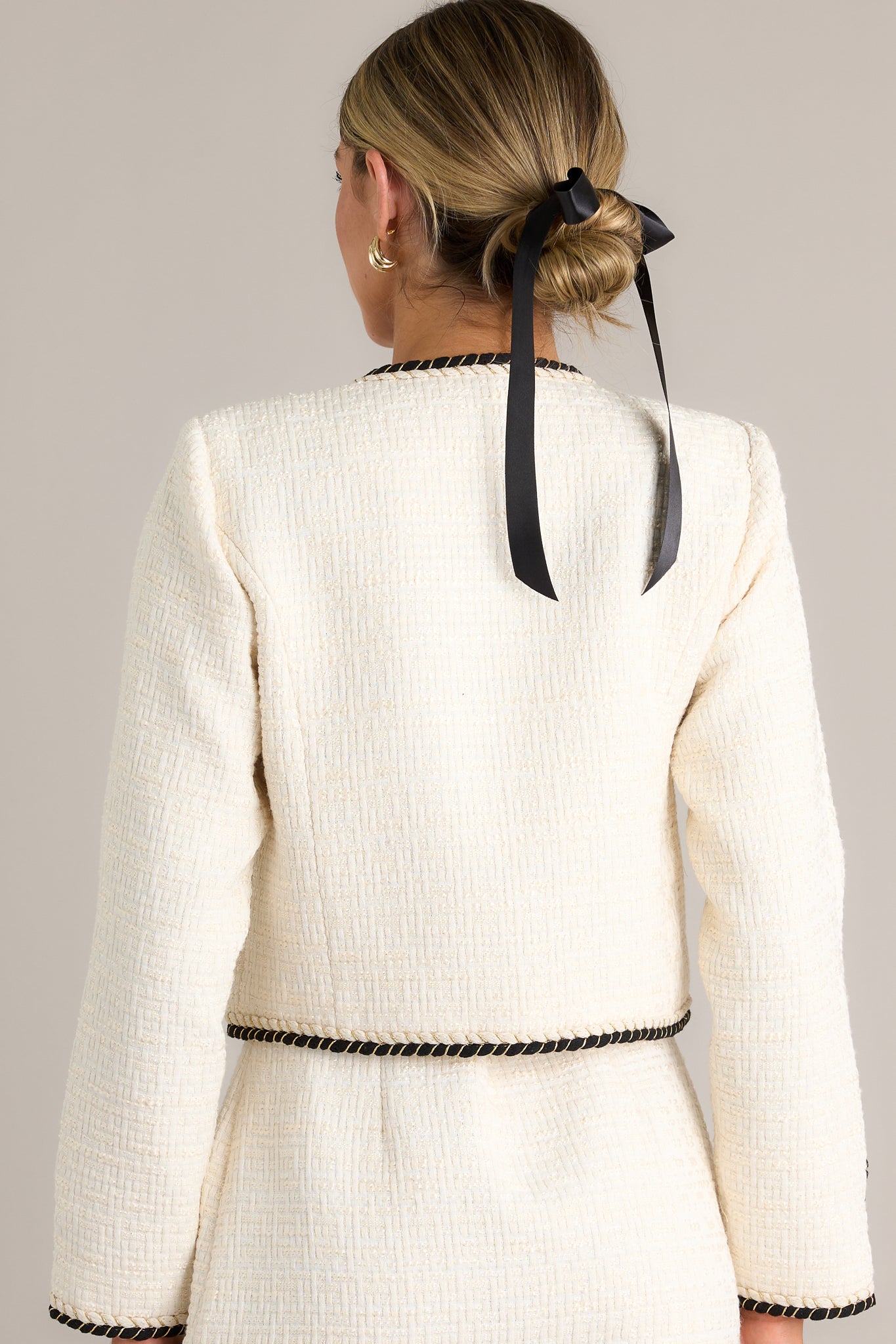 Back view of this ivory tweed jacket featuring a round neckline, a functional button front, functional pockets, a cropped design, monochrome braided trim, gold accent buttons and button cuffs.