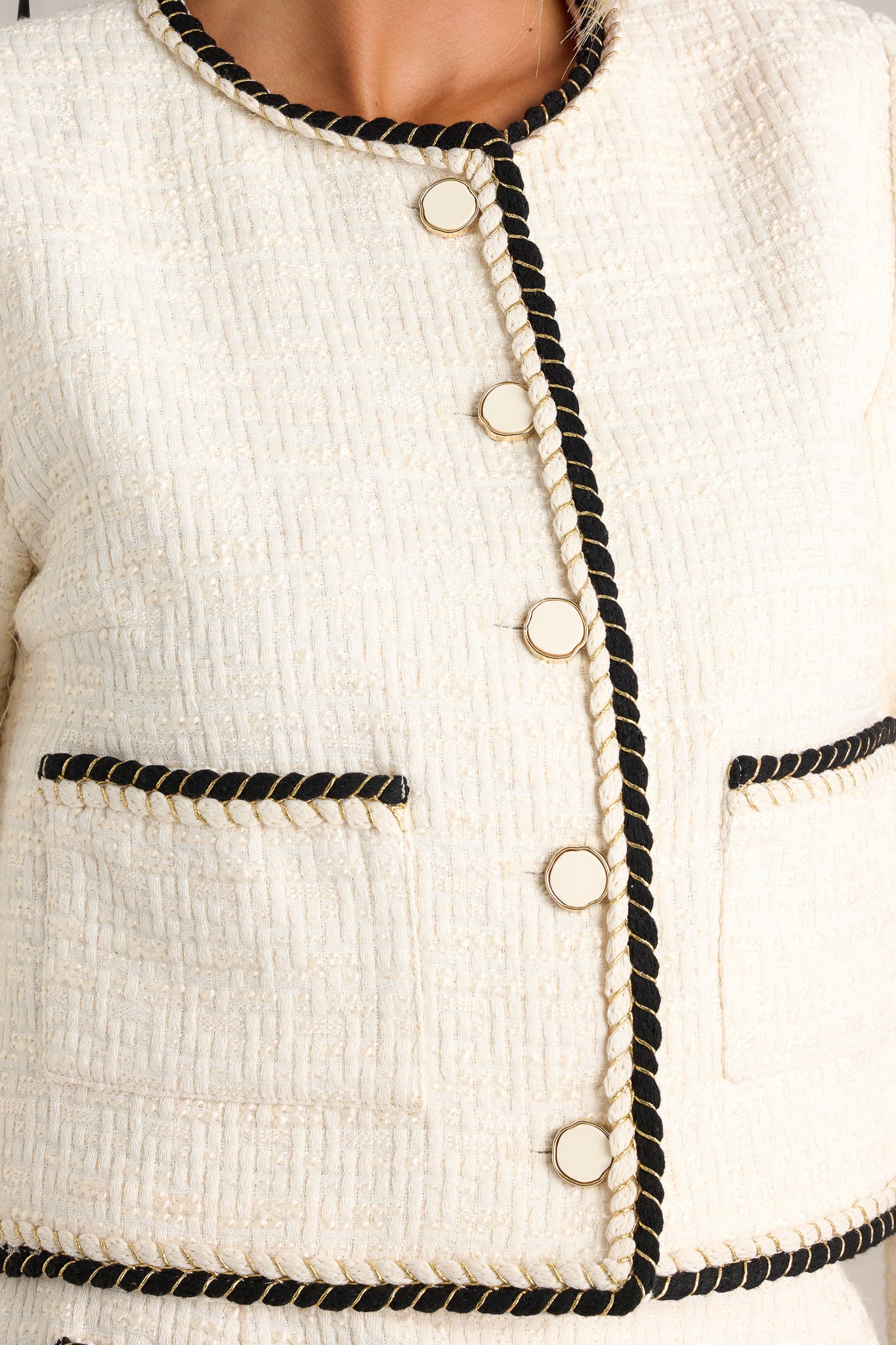 Detail shot of the gold trimmed ivory buttons, ivory and black braided trim, and pockets on this ivory tweed cropped jacket. 