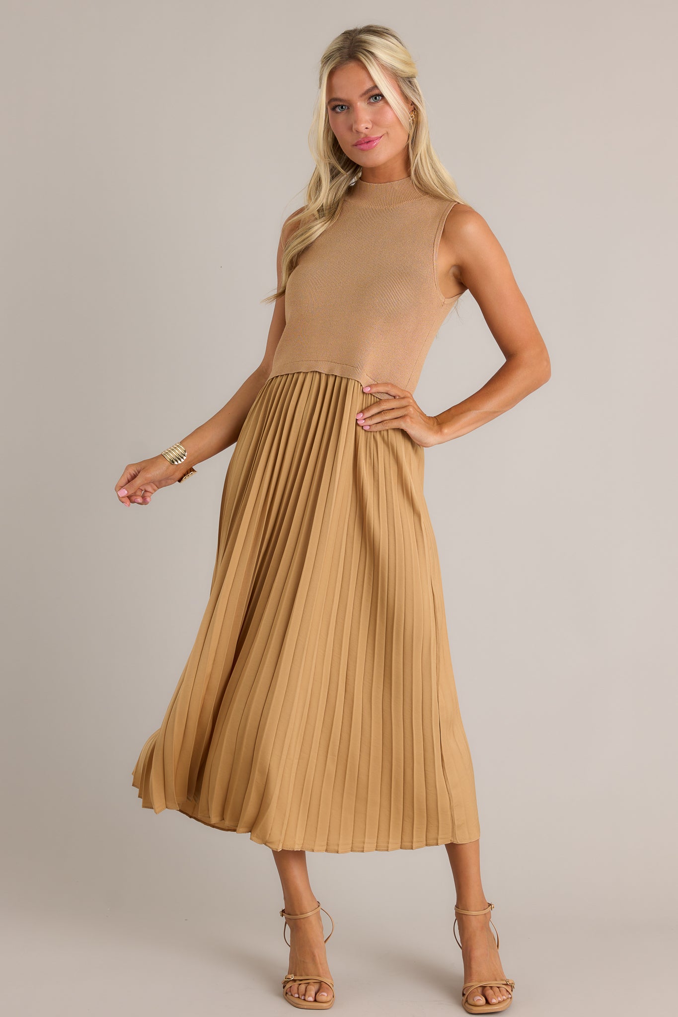 This mustard sleeveless dress features a high neckline, a ribbed knit bodice, a pleated skirt, a sleeveless design and a flowing silhouette.