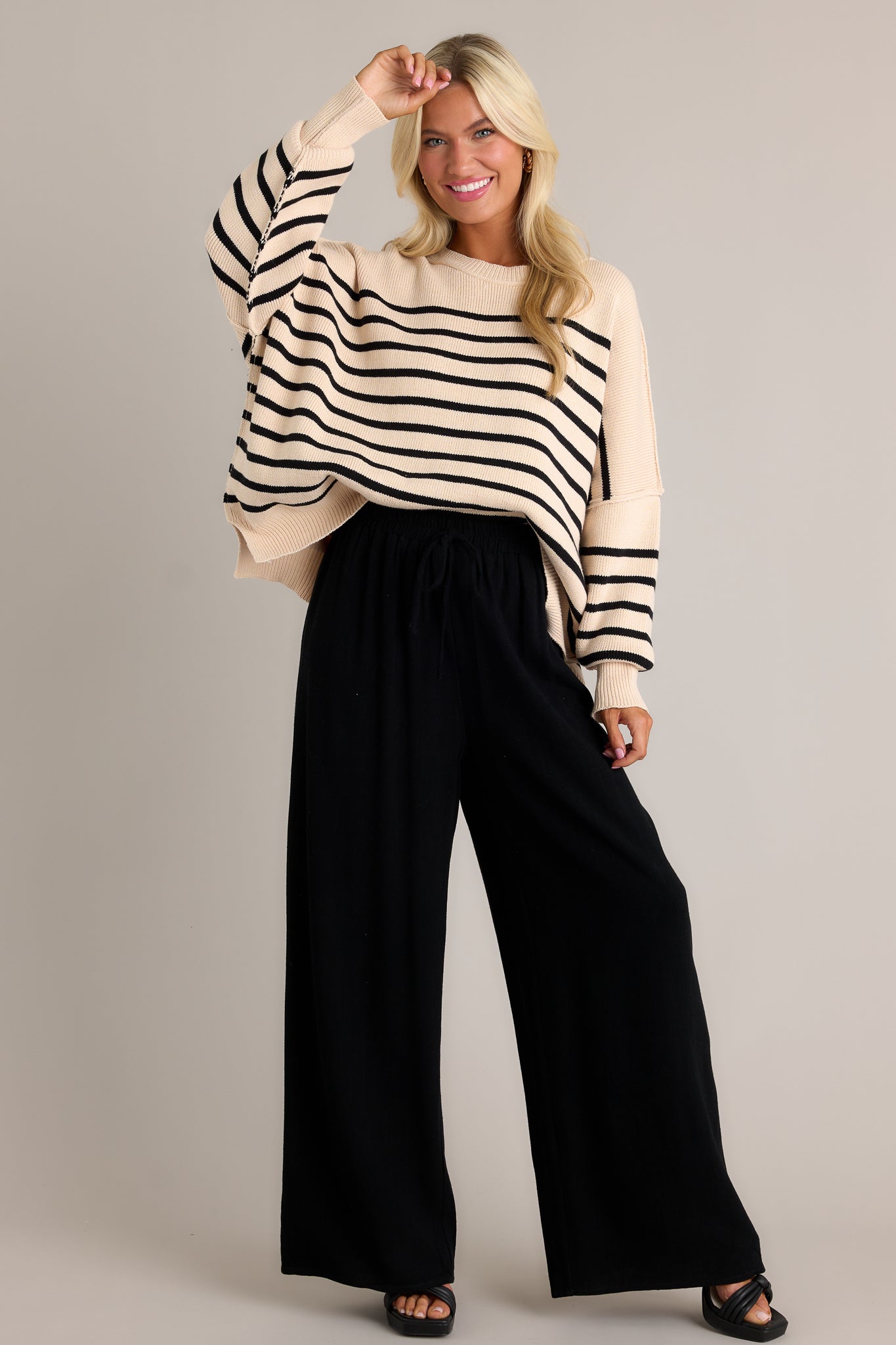 Full body view of these black pants that feature a high waisted design, an elastic waistband, a self-tie waist feature, and a wide leg.