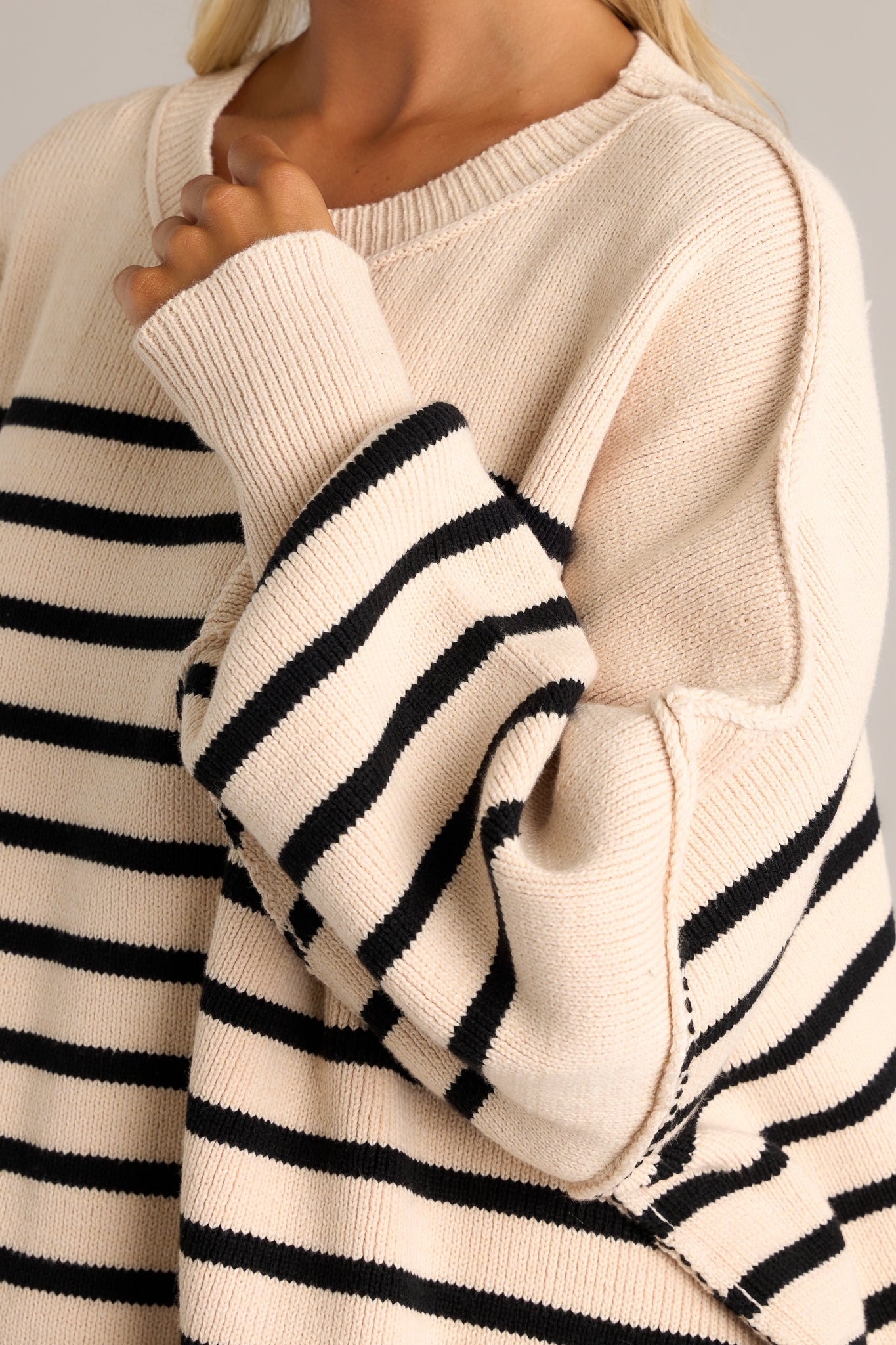 Detail shot of the tight cuff and oversized sleeves on this beige striped knit sweater.