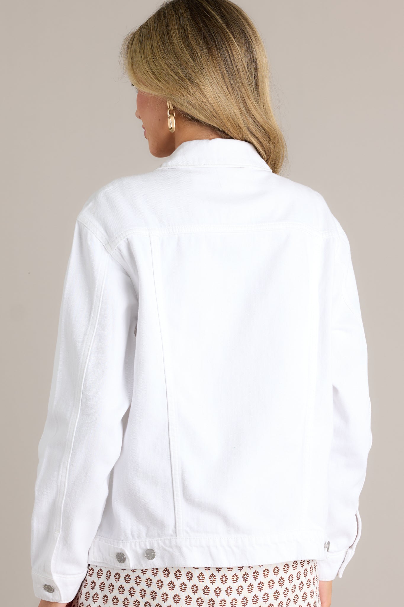 Back view of a white denim jacket highlighting the overall fit, white collar, and button sleeves.