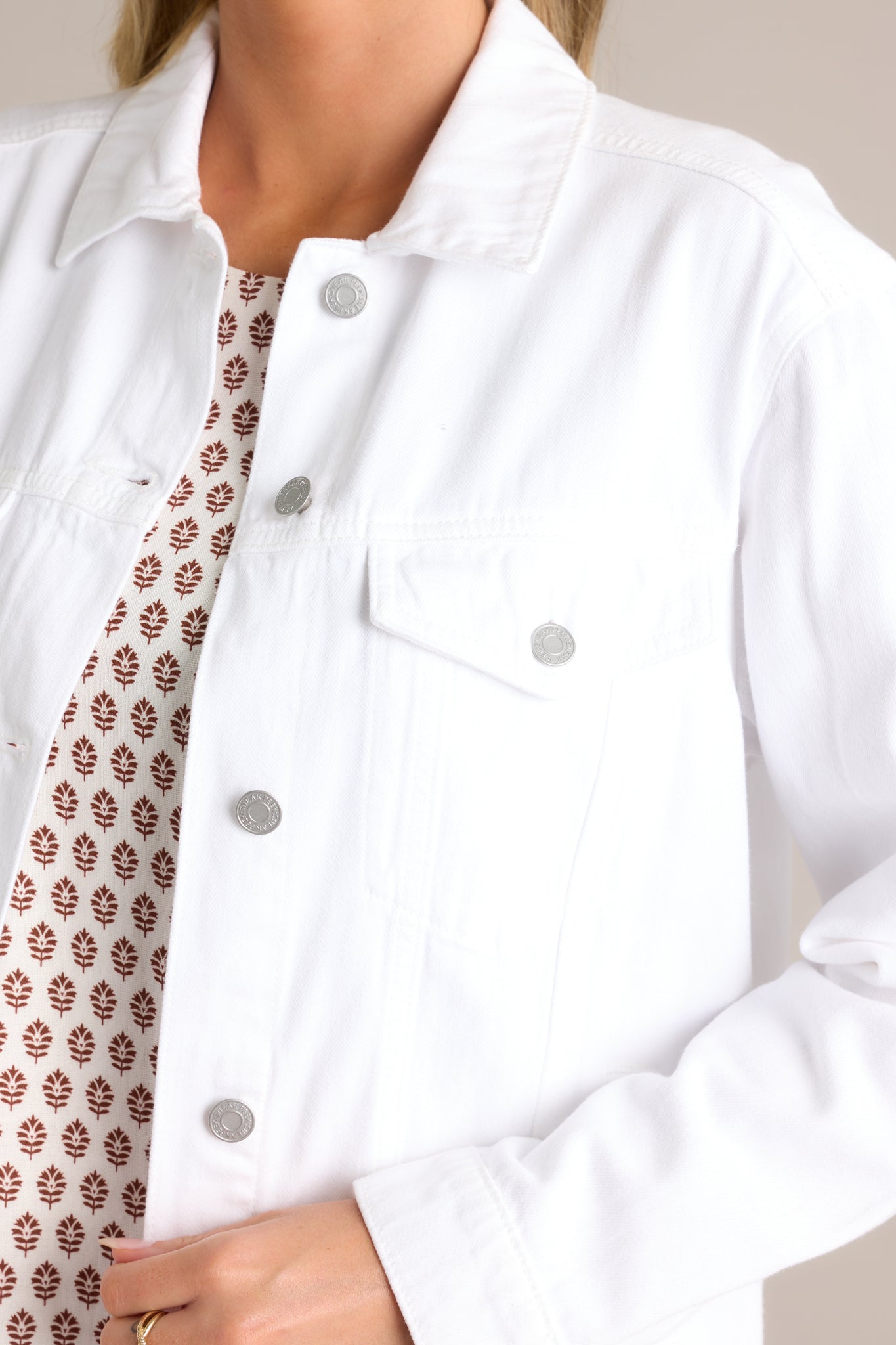 Close-up of the white denim jacket showing the white collar, functional button front, and chest pockets.