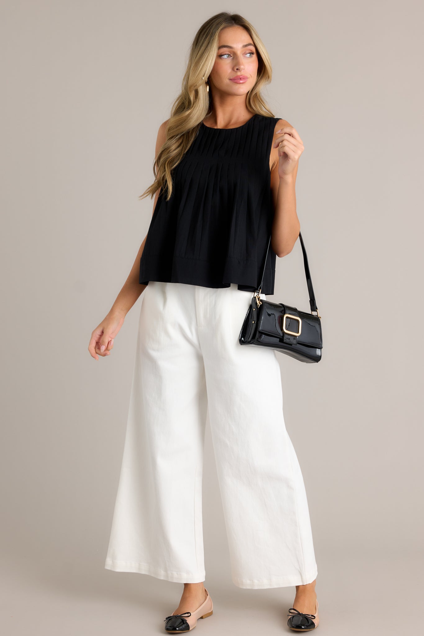 Full length view of the sleeveless black top featuring a round neckline, pleated bust, a slightly pleated bodice, a relaxed fit, and a sleeveless design