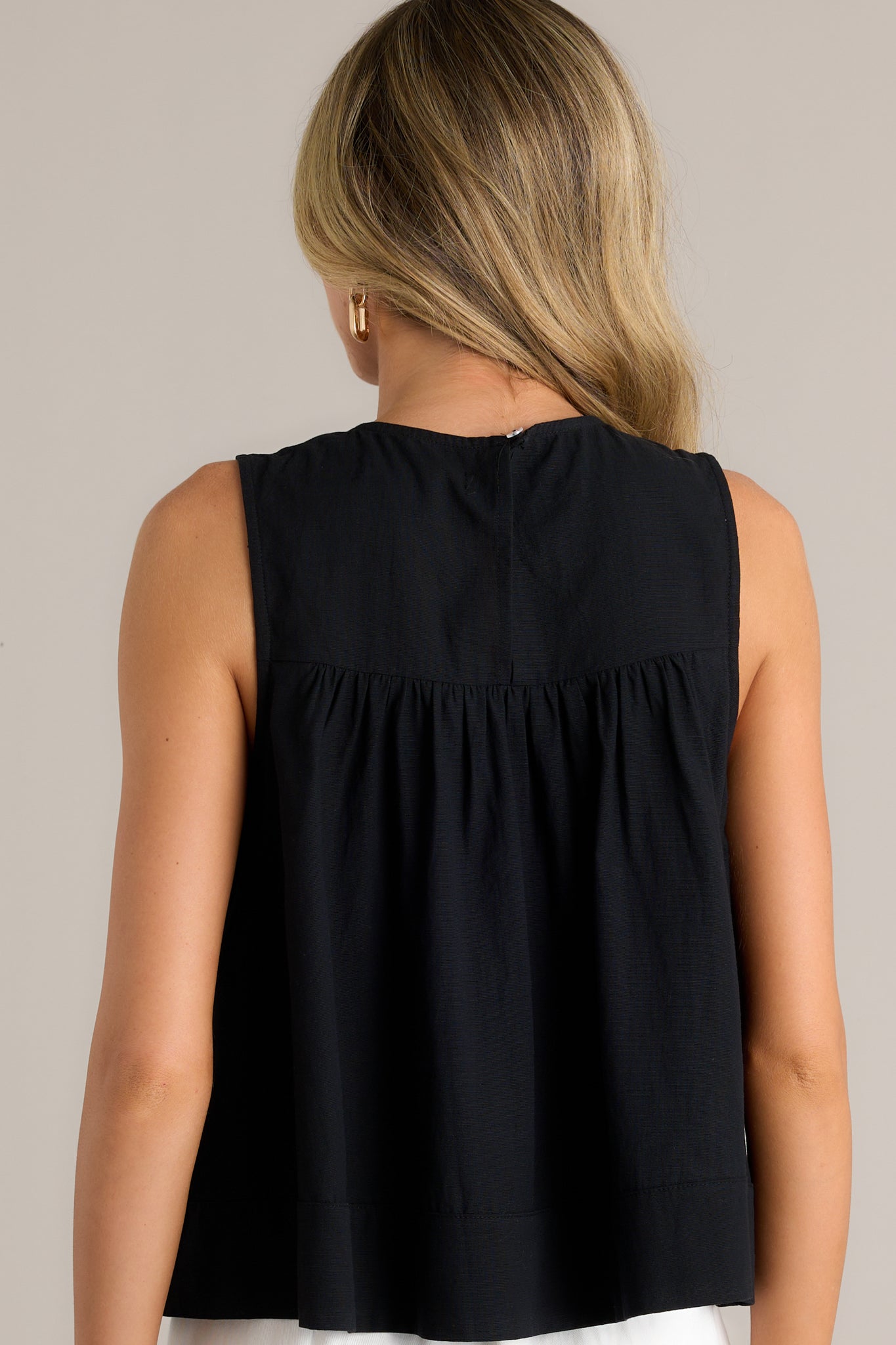 Back view of the sleeveless black top highlighting the smooth back and the relaxed fit of the bodice.