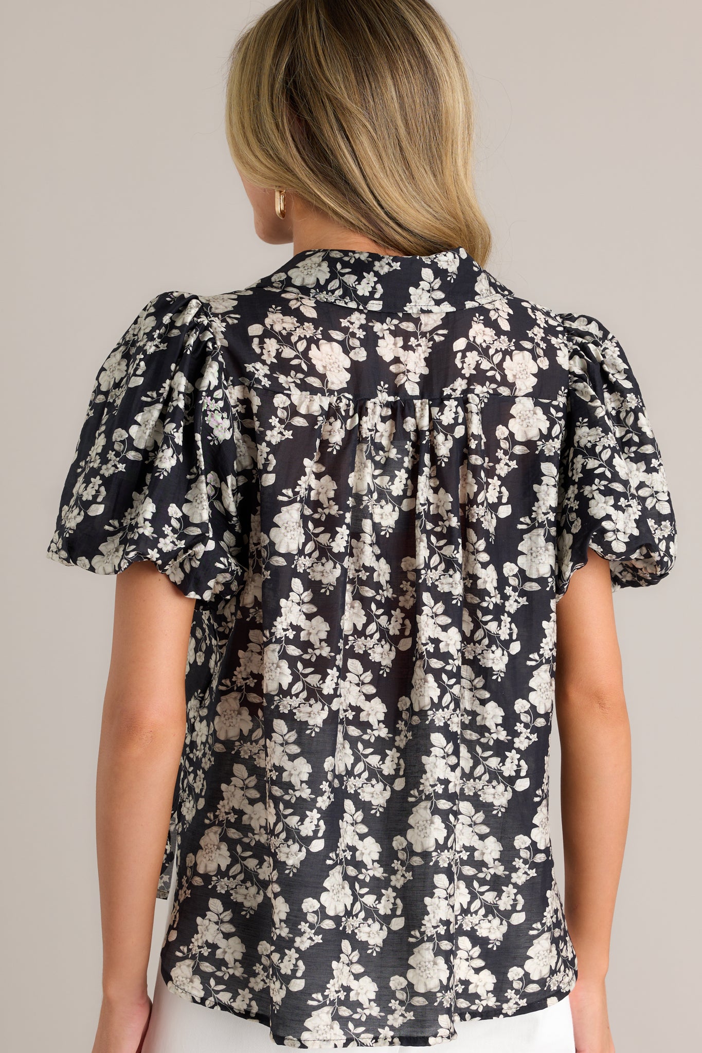 Back view of a black floral top with short elastic cuffed puff sleeves, showing the floral pattern and side slits in the hem.