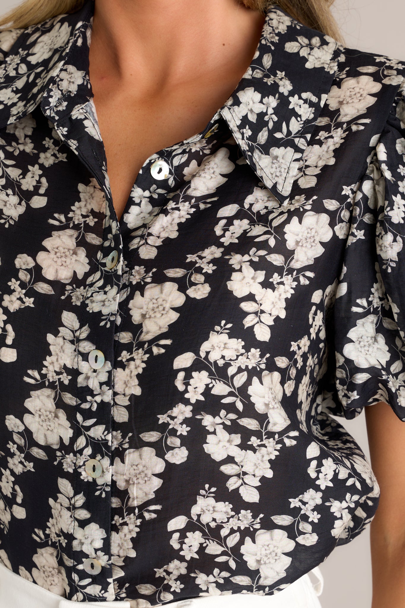 Close-up detail of a black floral top highlighting the collared high neckline, functional button front, and floral pattern.